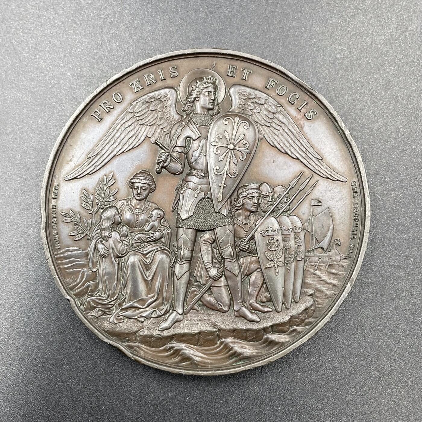 「木头集藏」章牌专场-第67场 1881年英国志愿兵运动21周年纪念铜章，直径：63.5mm，93.8 g，中央刻画天使长米迦勒（St. Michael），他身披盔甲、手持盾牌与宝剑，象征着守护与勇气。左侧是怀抱孩子的母亲与少女，手持橄榄枝，代表家园与和平；右侧是跪姿的志愿兵与列队士兵，背景还有帆船，呼应了志愿兵海陆防御的职责。