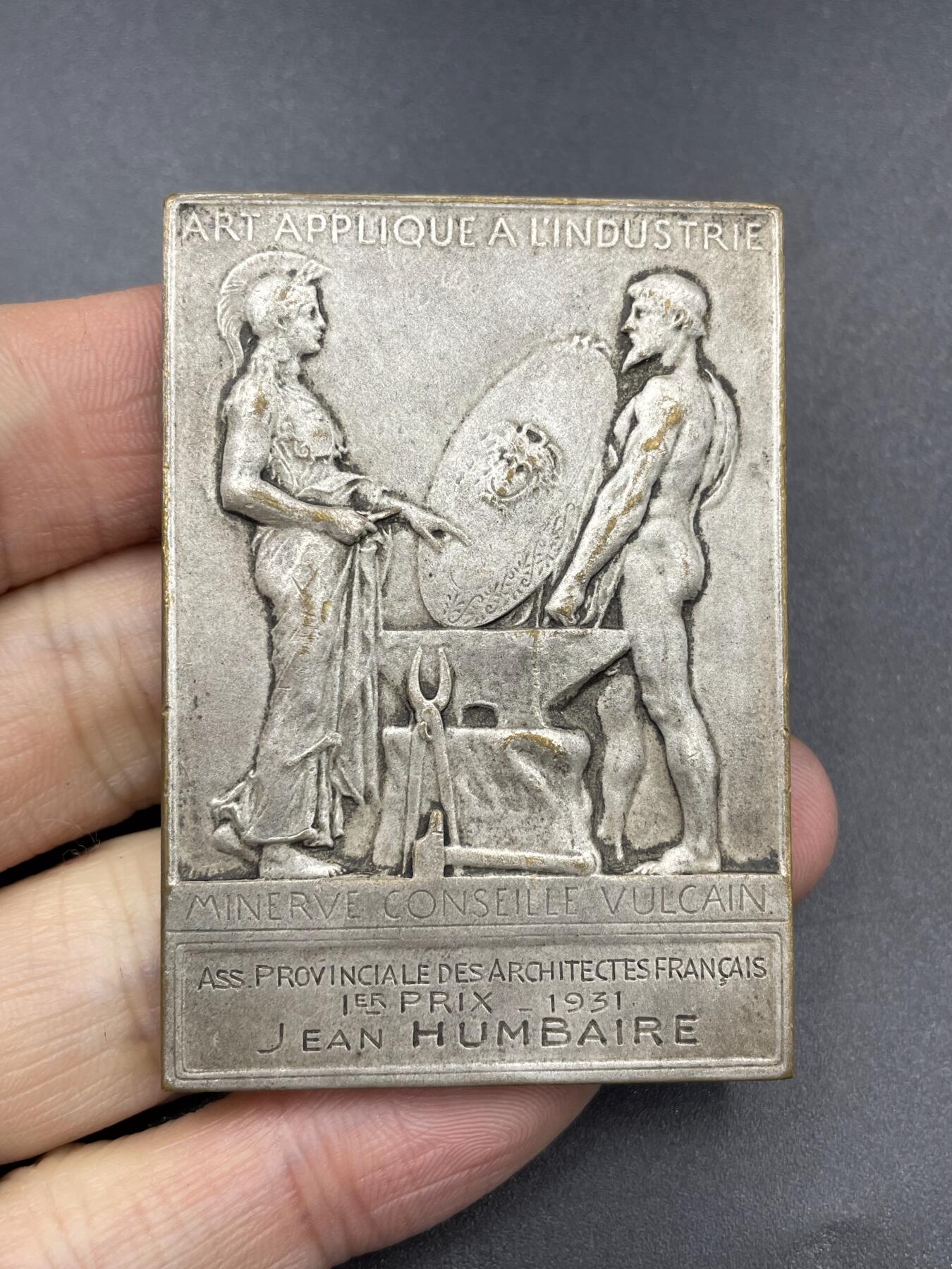 「木头集藏」章牌专场-第67场 O.Roty～法国艺术与工业促进会镀银章，尺寸：42 × 60 mm ，73 g，边铭：丰饶角 BRONZE， 此章正面采用了罗蒂经典的戎装玛丽安娜头像。上方是法语“法兰西共和国”，下方是“艺术与工业促进会”铭文。背面图案为古希腊神话中掌管火、锻造与工匠技艺的赫菲斯托斯，在向智慧女神雅典娜展示将美杜莎头颅镶嵌上去的盾牌。上方铭文