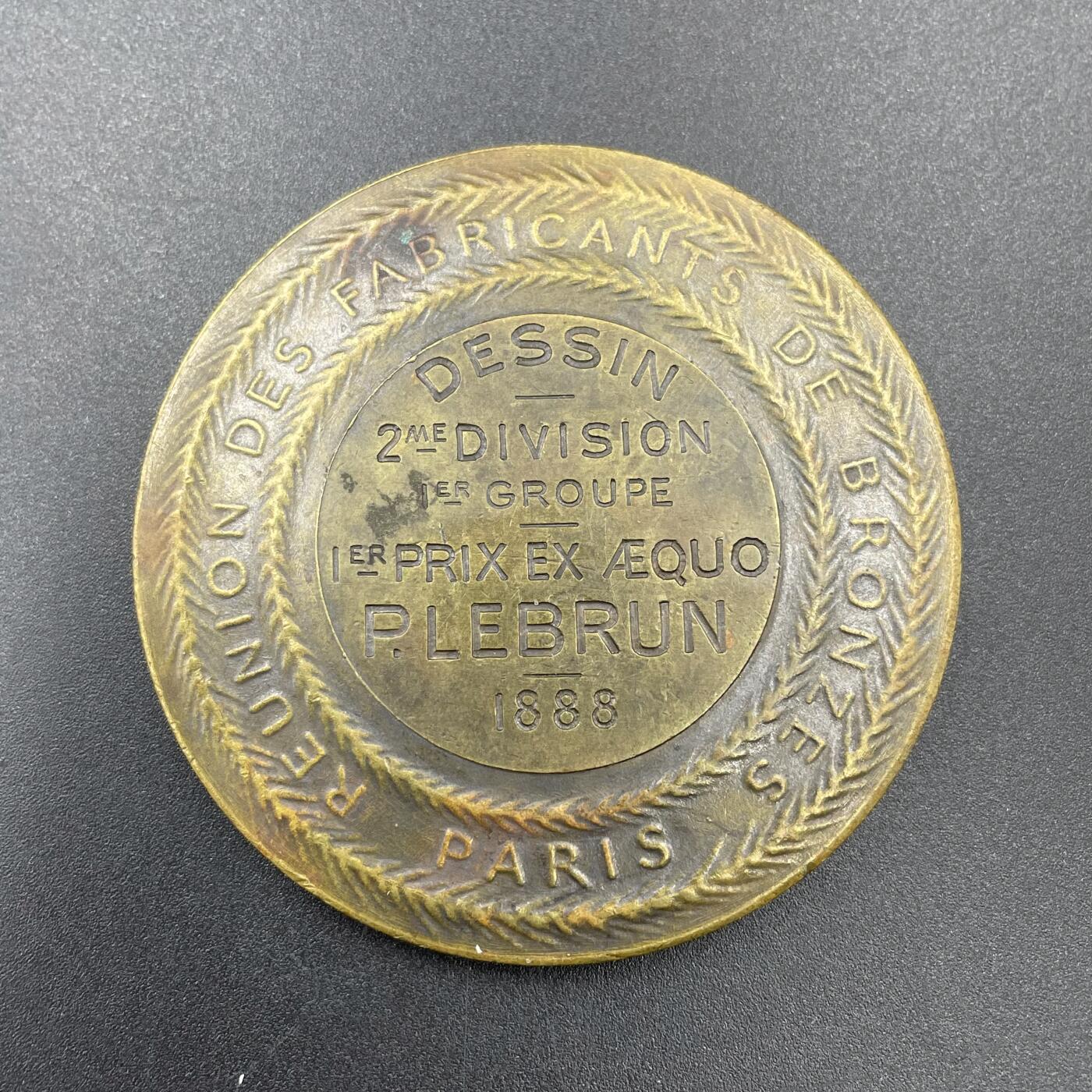 「木头集藏」章牌专场-第67场 F Levillain～1888年法国火神赫淮斯托斯为宙斯打造盾牌铜章 ，直径：58mm，边铭：丰饶角 BRONZE，马耶尔目录（1870-1940年法国章牌艺术）126号作品。背面铭文显示此章是巴黎青铜制造商协会颁发给绘画比赛并列第一名的P. Lebrun。正面是正在打造宙斯盾牌的赫淮斯托斯。赫淮斯托斯是宙斯和赫拉的儿子，希腊神话中的火神和匠神，为诸神打造了很多兵器。