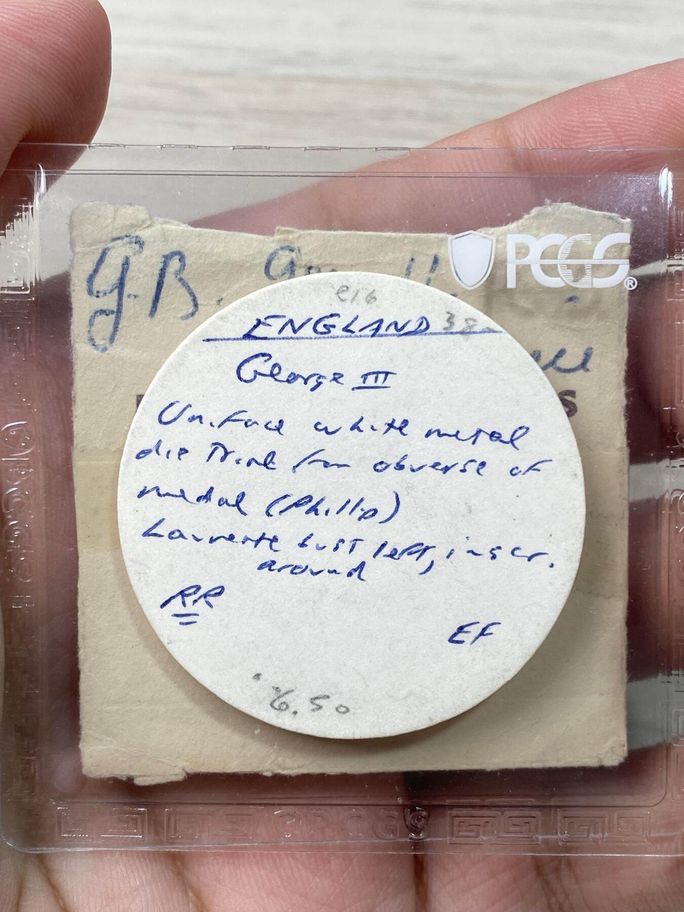 万国钱币拍卖第060期（万国六十期纪念大拍）  PCGS MS63 1811年英格兰银行系列乔治三世1元样币-正面铸样 经过改动后此头像被用于5先令又6便士的样币上。理查德·马乔里旧藏，法国与英国SOHO MINT铸币的专家，1958年成为币商，后期设计铸造了大名鼎鼎的古巴流亡政府少女比索银币，最后被美国政府查抄模具而收场。他上世纪60年代以来购买的出自包括法鲁克国王、苏尔曼等顶级集藏的英法藏品近两年来屡屡排出高价。附带原标签和纸袋。