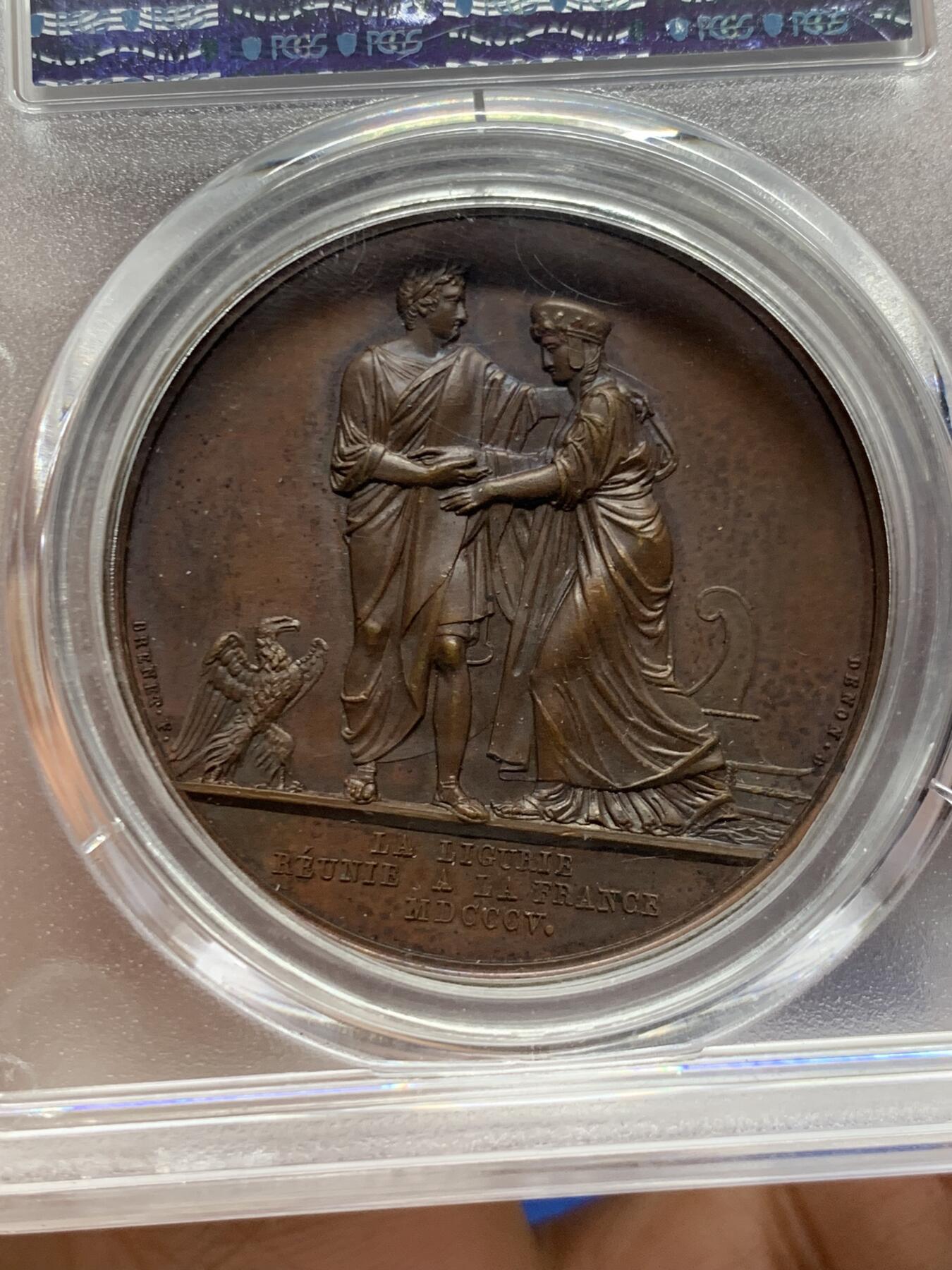 《竞宝斋》第463-465场 周日，周一，周二，3场连拍 （全场包邮）欢迎送拍 PCGS SP64 亚军分 法国1805年拿破仑一世吞并利古里亚原铸铜章 巴黎造币厂 巧克力包浆 左边拿破仑身穿古罗马元老院服饰cos凯撒，接受右边着罗马将军长袍的利古里亚首领低头屈服，两侧饰有象征性的鹰和船头，记录着拿皇攻城略地的丰功伟绩，衣服缕缕毕现生动刻画，人像稀少品种，加厚盒，标签可晃动。仅一枚更高分