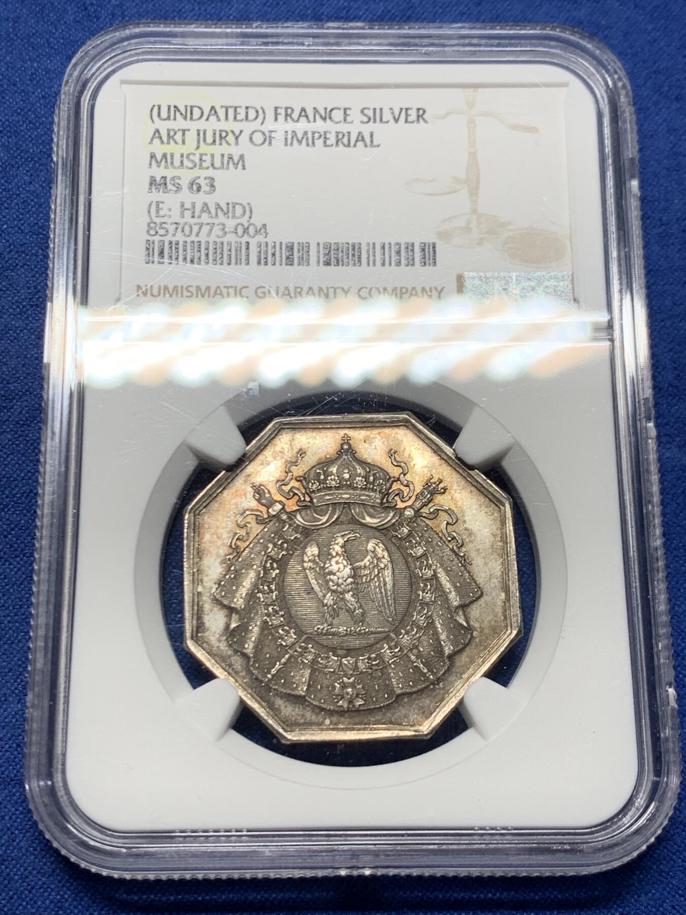 《竞宝斋》第463-465场 周日，周一，周二，3场连拍 （全场包邮）欢迎送拍 NGC MS63 帝国博物馆艺术评审团（Art Jury of Imperial Museum）银质八角代币，正面中央为帝国鹰徽，鹰立于盾徽之上，盾徽外覆披风并加冕皇冠，周围辅以勋章、绶带与权杖元素，构成完整的帝国象征体。