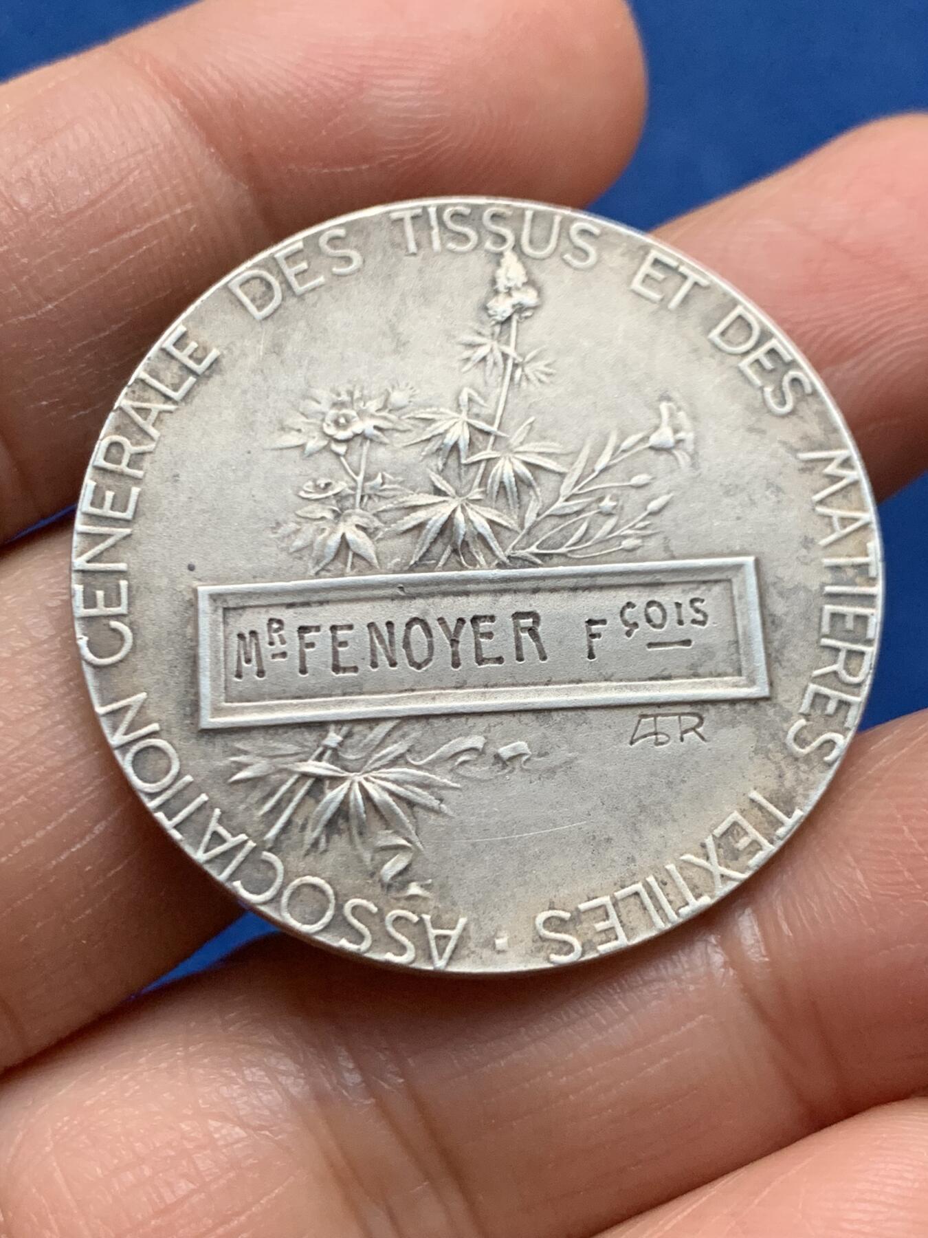 《竞宝斋》第463-465场 周日，周一，周二，3场连拍 （全场包邮）欢迎送拍 法兰西纺织总协会银质奖章，银章本体大约铸造于20世纪初期，此枚无加刻颁奖年版，推测授奖颁发时段在1900-1940年间，中央饰框内刻有得奖者名称“Mr Fenoyer/费诺耶先生”，  雕刻师：A. RIVET阿道夫·里韦，边缘ARGENT 950银标/丰饶角。重约20.6克。