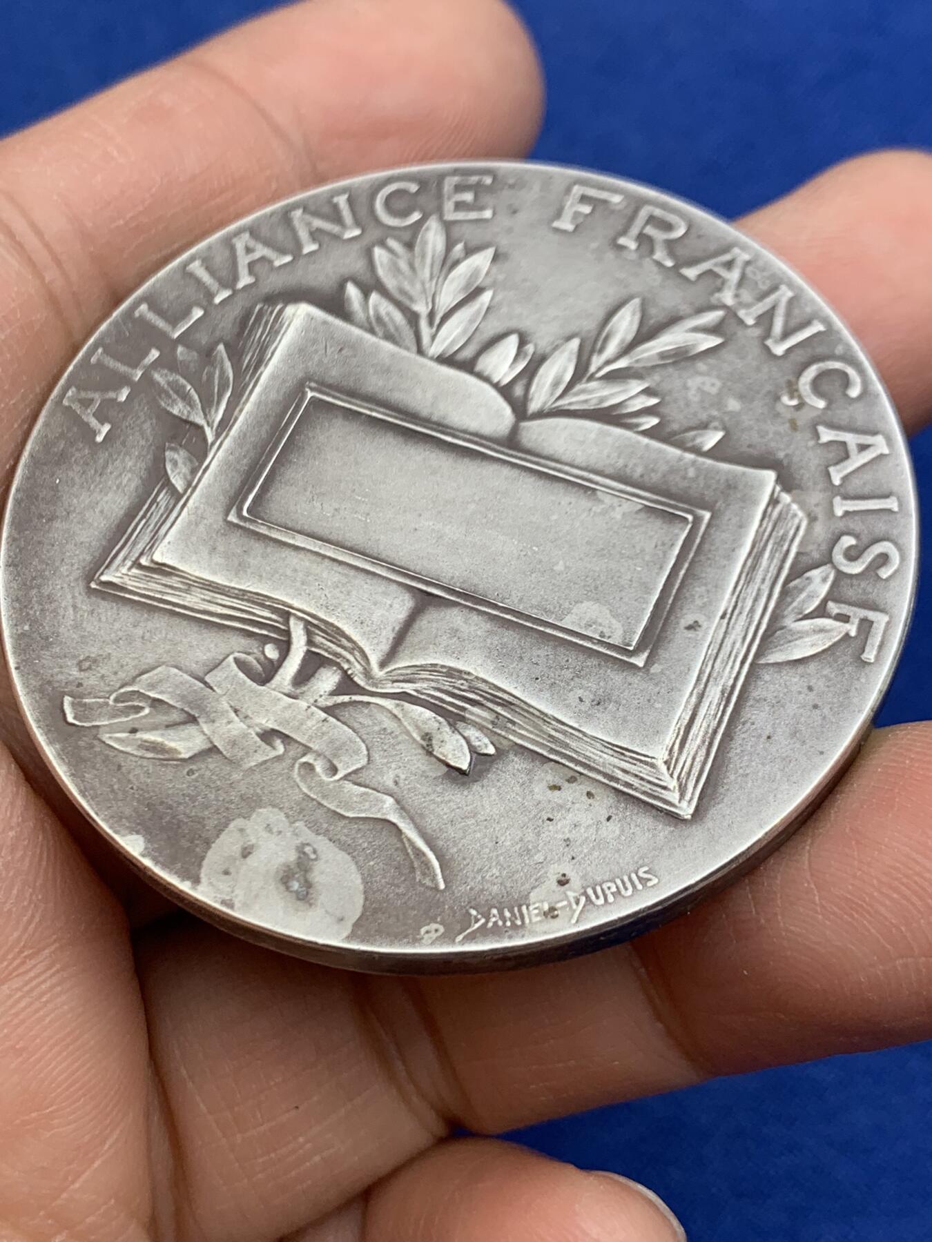 《竞宝斋》第464场 周日，周一，周二，3场连拍 （全场包邮）欢迎送拍 法国新艺术章牌雕刻大师杜普伊D.Dupuis作品，法语联盟奖章，法国的象征玛丽安娜女神，在月桂树下教美澳亚非四大洲的孩子读书，写实浅浮雕精品。小小的章面上，能把四大洲孩子的衣着甚至面部特色都生动表现出来，绝对是大师级雕刻功力，材质950银，边铭丰饶角argent，直径50mm，重量66g，品相很好，包浆有轻微白斑，自藏佳品