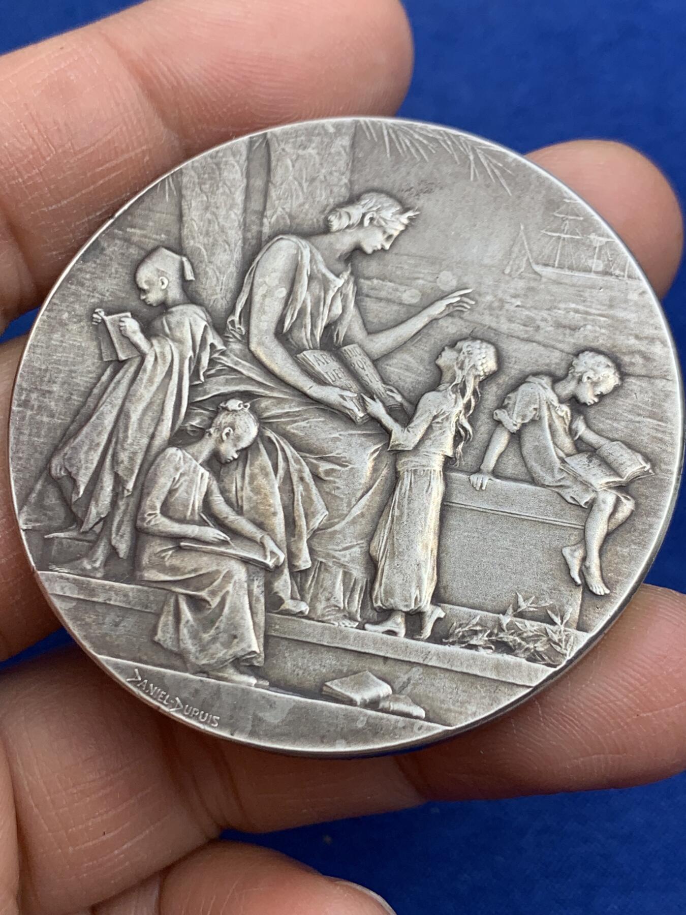 《竞宝斋》第464场 周日，周一，周二，3场连拍 （全场包邮）欢迎送拍 法国新艺术章牌雕刻大师杜普伊D.Dupuis作品，法语联盟奖章，法国的象征玛丽安娜女神，在月桂树下教美澳亚非四大洲的孩子读书，写实浅浮雕精品。小小的章面上，能把四大洲孩子的衣着甚至面部特色都生动表现出来，绝对是大师级雕刻功力，材质950银，边铭丰饶角argent，直径50mm，重量66g，品相很好，包浆有轻微白斑，自藏佳品