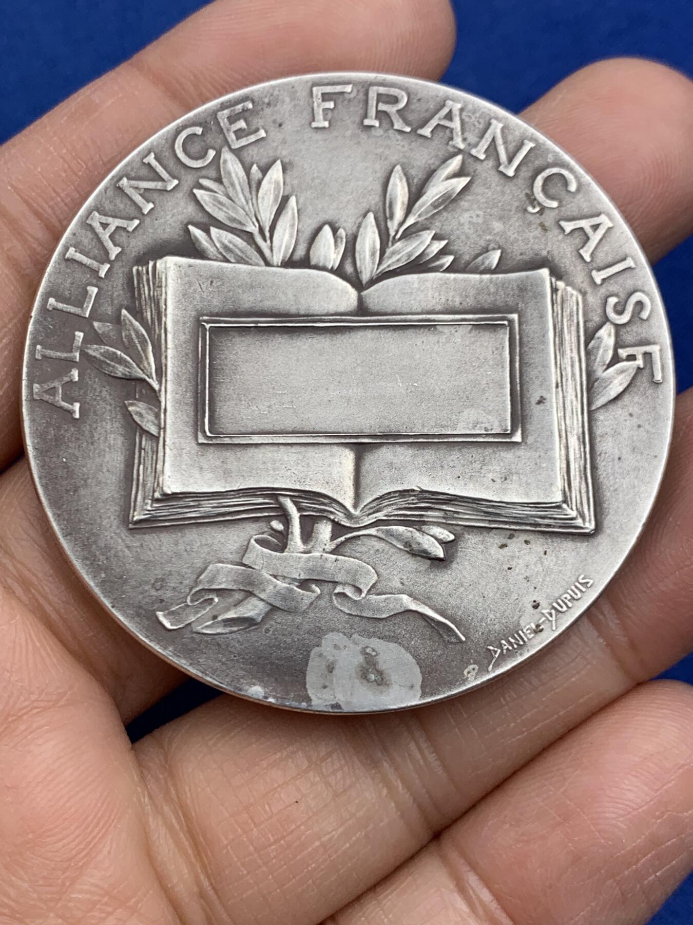 《竞宝斋》第464场 周日，周一，周二，3场连拍 （全场包邮）欢迎送拍 法国新艺术章牌雕刻大师杜普伊D.Dupuis作品，法语联盟奖章，法国的象征玛丽安娜女神，在月桂树下教美澳亚非四大洲的孩子读书，写实浅浮雕精品。小小的章面上，能把四大洲孩子的衣着甚至面部特色都生动表现出来，绝对是大师级雕刻功力，材质950银，边铭丰饶角argent，直径50mm，重量66g，品相很好，包浆有轻微白斑，自藏佳品