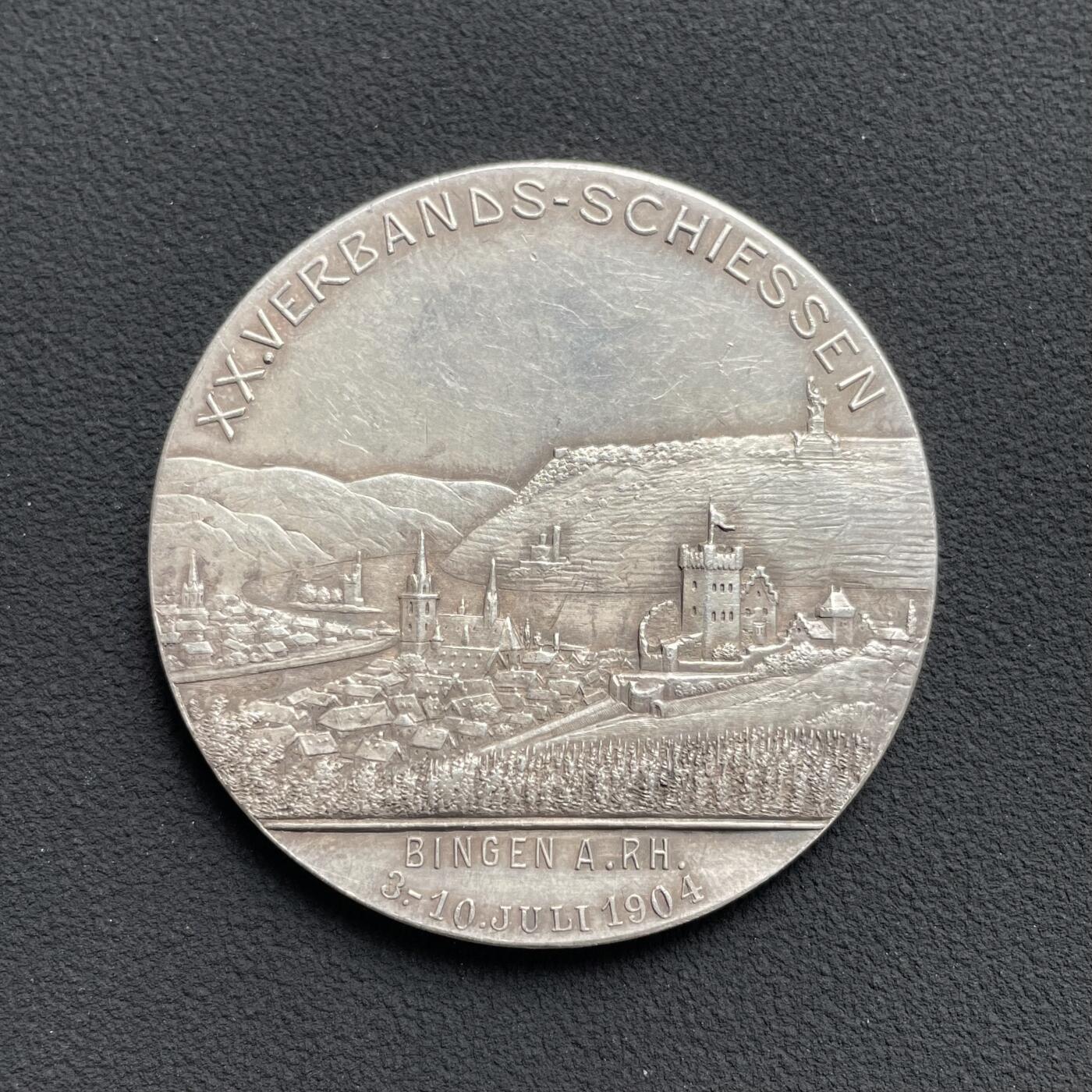 「木头集藏」“ 新岁撷珍”——章牌精品专场！ Balmberger～1904年德国宾根第20届协会射击节银章 ，直径：43 mm，35.5 g，少见品种，正面是黑森大公国恩斯特·路德维希大公的戎装像，背面是莱茵河畔的宾根城市景观，其中著名地标建筑包括河中小岛上的鼠塔，近处的圣马丁大教堂和克洛普城堡，以及远处山顶的尼德瓦尔德纪念碑。这座纪念碑是为纪念德国统一而建，基座上矗立着德意志国家的化身日耳曼尼亚女神。。