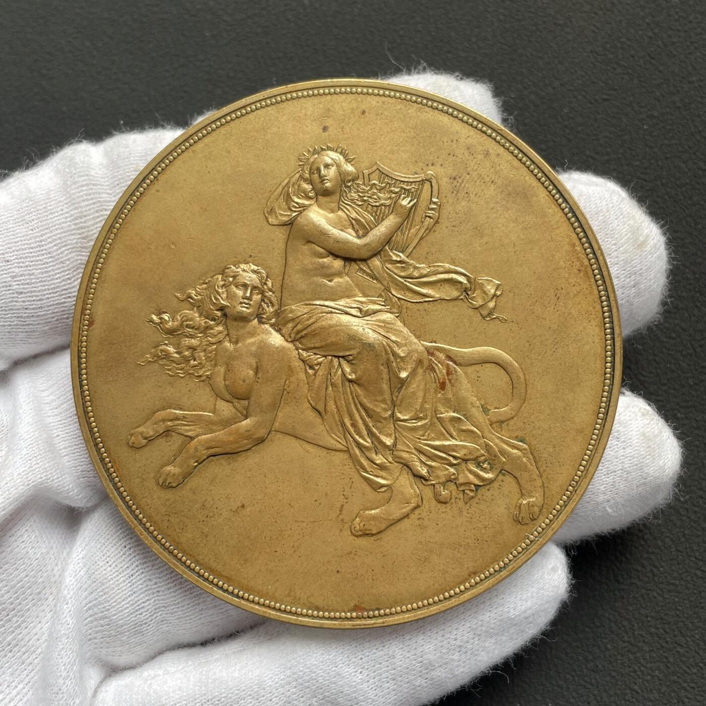 「木头集藏」“ 新岁撷珍”——章牌精品专场！   J. Tautenhayn～1891年德国 雕塑家黑内尔逝世纪念镀金铜章，直径：63 mm，112 g，罕见品种！由德国雕塑家席林和奥地利章牌大师陶滕海因联袂制作。正面是黑内尔肖像，背面半裸女神拨动琴弦，身下狮身人面的形象非常惊艳，兼具成熟女性的魅力与野兽的矫健。  恩斯特·尤利乌斯·黑内尔（1811-1891年）是19世纪德国最负盛名的雕塑家之一。