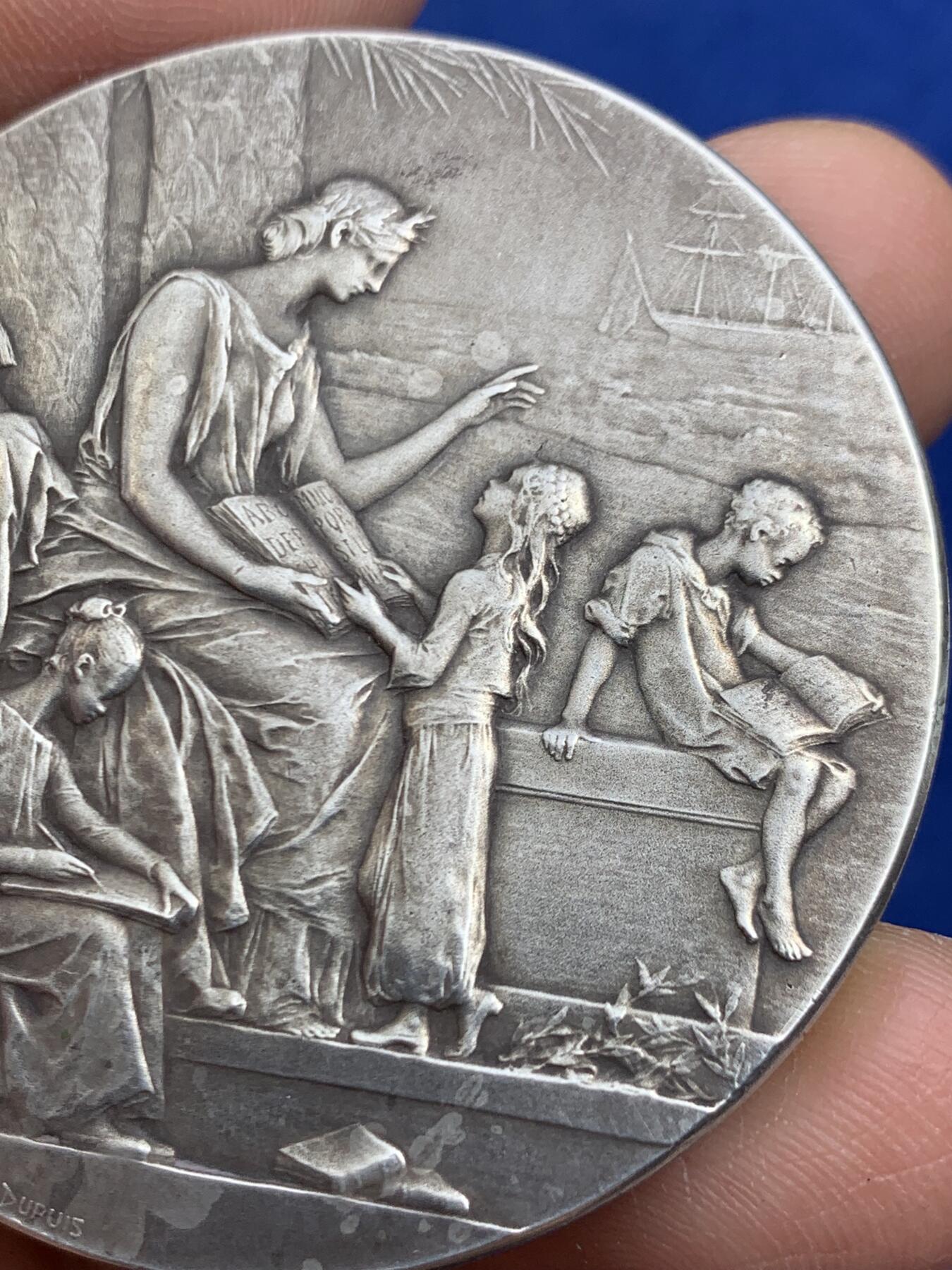 《竞宝斋》第464场 周日，周一，周二，3场连拍 （全场包邮）欢迎送拍 法国新艺术章牌雕刻大师杜普伊D.Dupuis作品，法语联盟奖章，法国的象征玛丽安娜女神，在月桂树下教美澳亚非四大洲的孩子读书，写实浅浮雕精品。小小的章面上，能把四大洲孩子的衣着甚至面部特色都生动表现出来，绝对是大师级雕刻功力，材质950银，边铭丰饶角argent，直径50mm，重量66g，品相很好，包浆有轻微白斑，自藏佳品