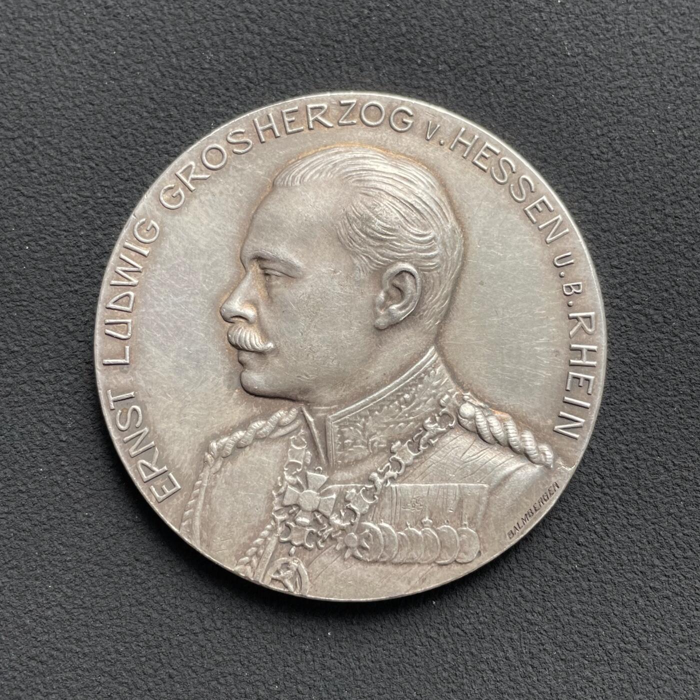 「木头集藏」“ 新岁撷珍”——章牌精品专场！ Balmberger～1904年德国宾根第20届协会射击节银章 ，直径：43 mm，35.5 g，少见品种，正面是黑森大公国恩斯特·路德维希大公的戎装像，背面是莱茵河畔的宾根城市景观，其中著名地标建筑包括河中小岛上的鼠塔，近处的圣马丁大教堂和克洛普城堡，以及远处山顶的尼德瓦尔德纪念碑。这座纪念碑是为纪念德国统一而建，基座上矗立着德意志国家的化身日耳曼尼亚女神。。