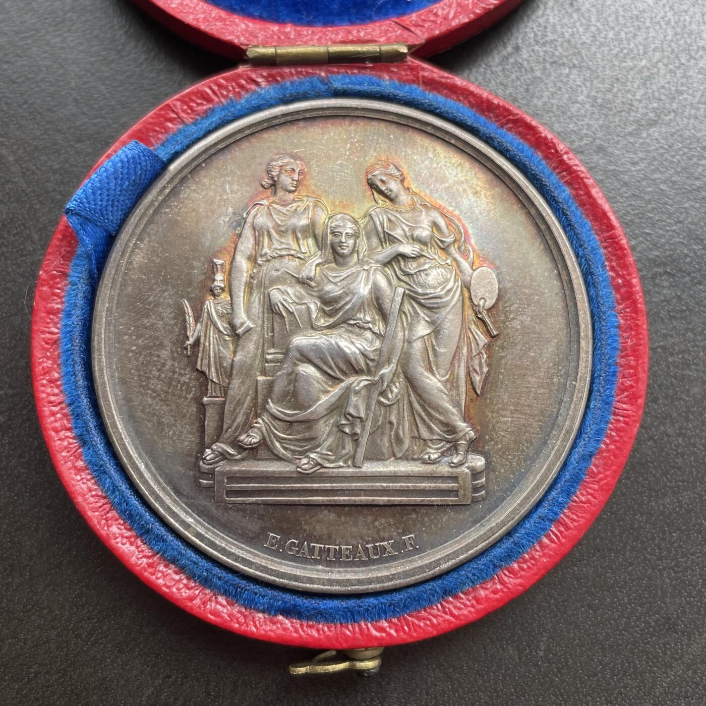 「木头集藏」“ 新岁撷珍”——章牌精品专场！ 1902年法国巴黎国立高等美术学院原盒银章，直径：41 mm，37 g，边铭：丰饶角 ARGENT，三位女性分别代表雕塑（手持锤子与凿子）、建筑（手持标尺与绘图工具）、绘画（手持调色板与画笔）。 左侧小雕像为智慧女神密涅瓦（Minerva），代表艺术创作的理性与灵感。品相不错，彩色氧化很美，原盒正常使用，同款收藏佳品。