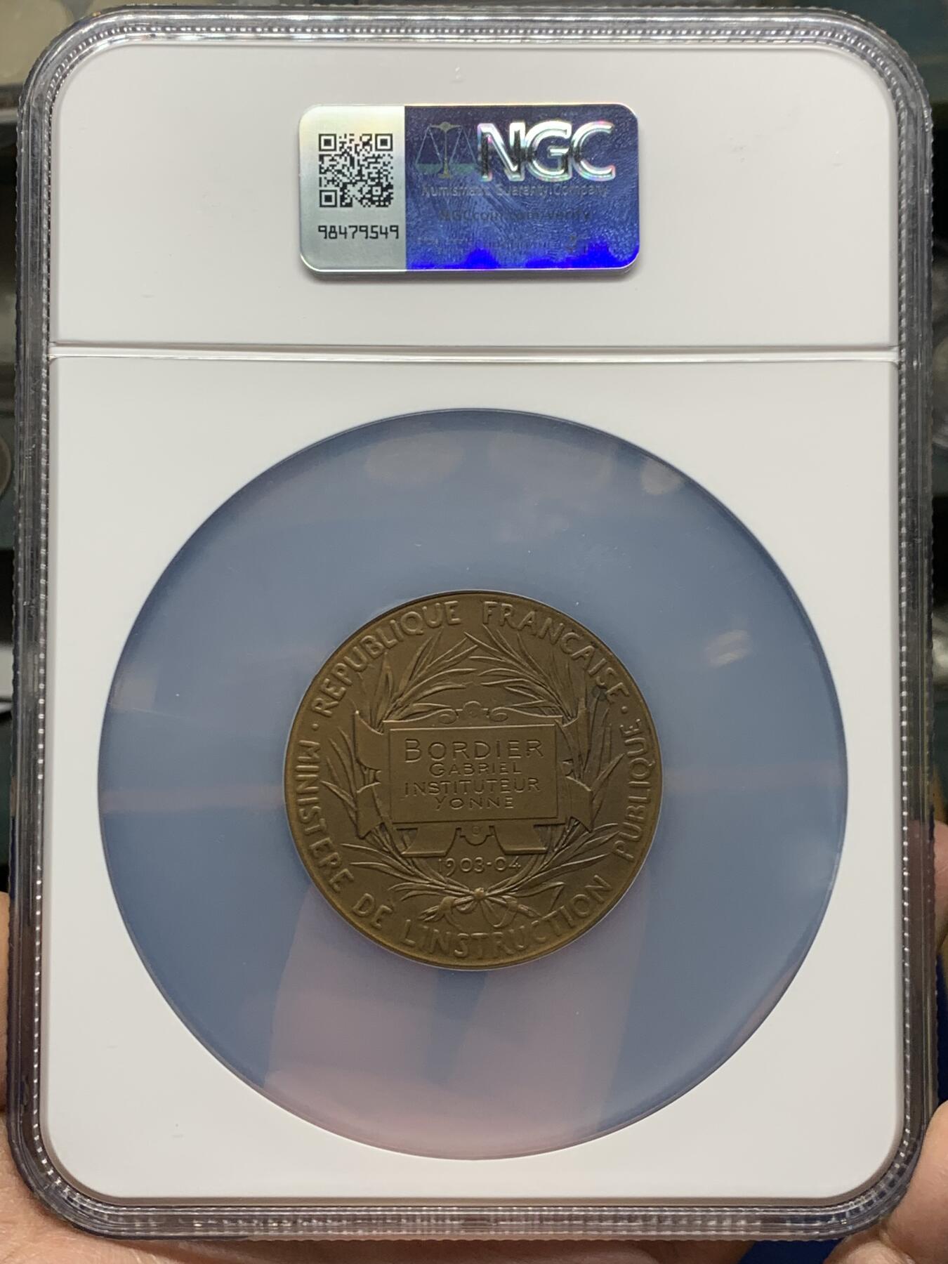 《竞宝斋》第465场 周日，周一，周二，3场连拍 （全场包邮）欢迎送拍 NGC MS64BN 1904年法国初级教育铜章，罗蒂作品，直径51毫米，正面图案展现了一位女性教师向两名学生传授知识的场景，象征着国家对基础教育的重视。加大盒
