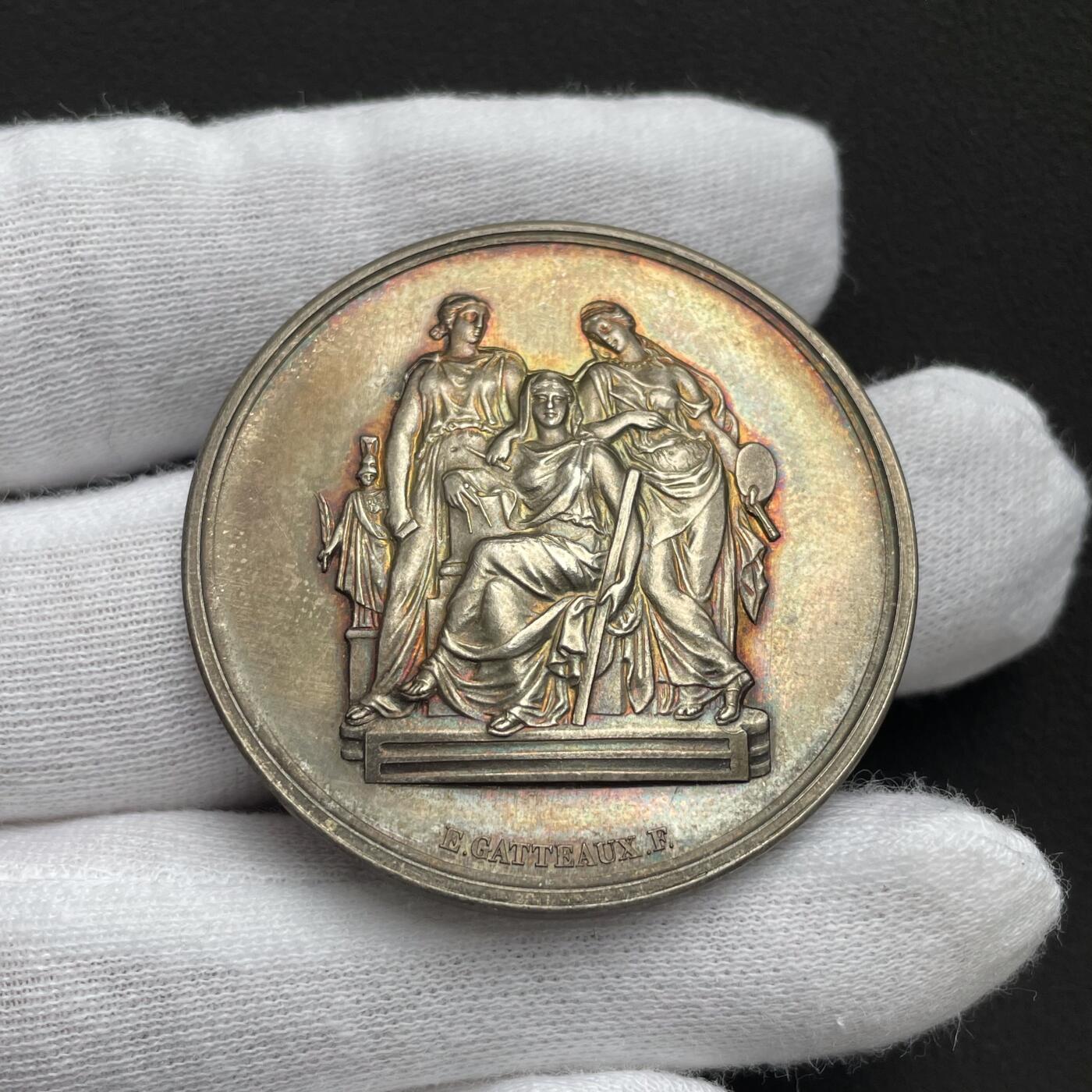 「木头集藏」“ 新岁撷珍”——章牌精品专场！ 1902年法国巴黎国立高等美术学院原盒银章，直径：41 mm，37 g，边铭：丰饶角 ARGENT，三位女性分别代表雕塑（手持锤子与凿子）、建筑（手持标尺与绘图工具）、绘画（手持调色板与画笔）。 左侧小雕像为智慧女神密涅瓦（Minerva），代表艺术创作的理性与灵感。品相不错，彩色氧化很美，原盒正常使用，同款收藏佳品。