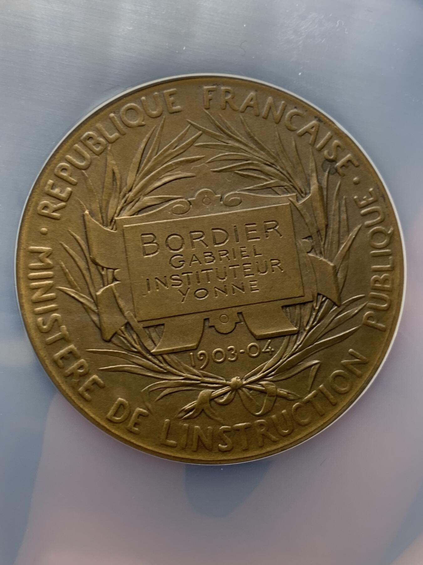 《竞宝斋》第465场 周日，周一，周二，3场连拍 （全场包邮）欢迎送拍 NGC MS64BN 1904年法国初级教育铜章，罗蒂作品，直径51毫米，正面图案展现了一位女性教师向两名学生传授知识的场景，象征着国家对基础教育的重视。加大盒