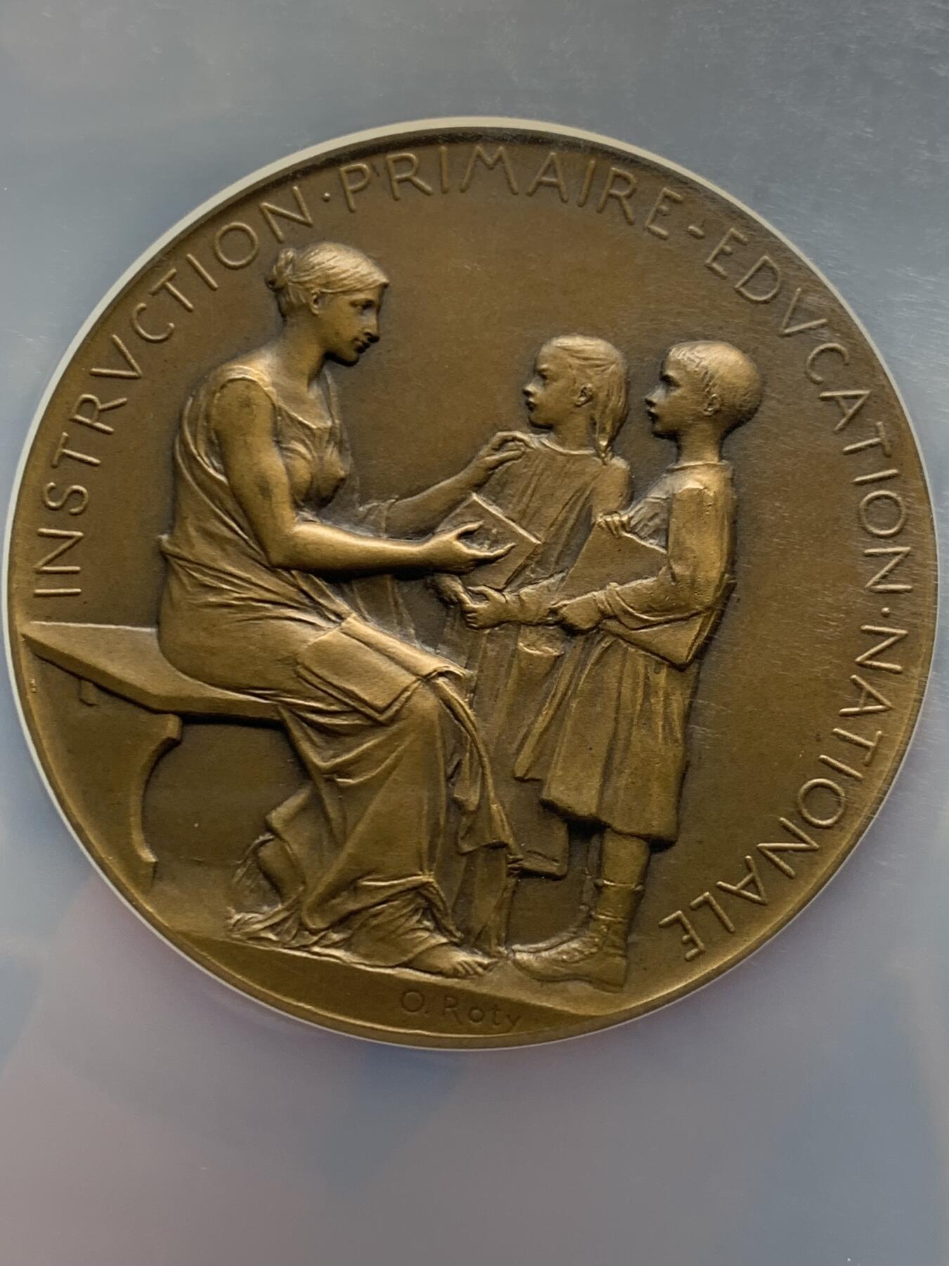 《竞宝斋》第465场 周日，周一，周二，3场连拍 （全场包邮）欢迎送拍 NGC MS64BN 1904年法国初级教育铜章，罗蒂作品，直径51毫米，正面图案展现了一位女性教师向两名学生传授知识的场景，象征着国家对基础教育的重视。加大盒