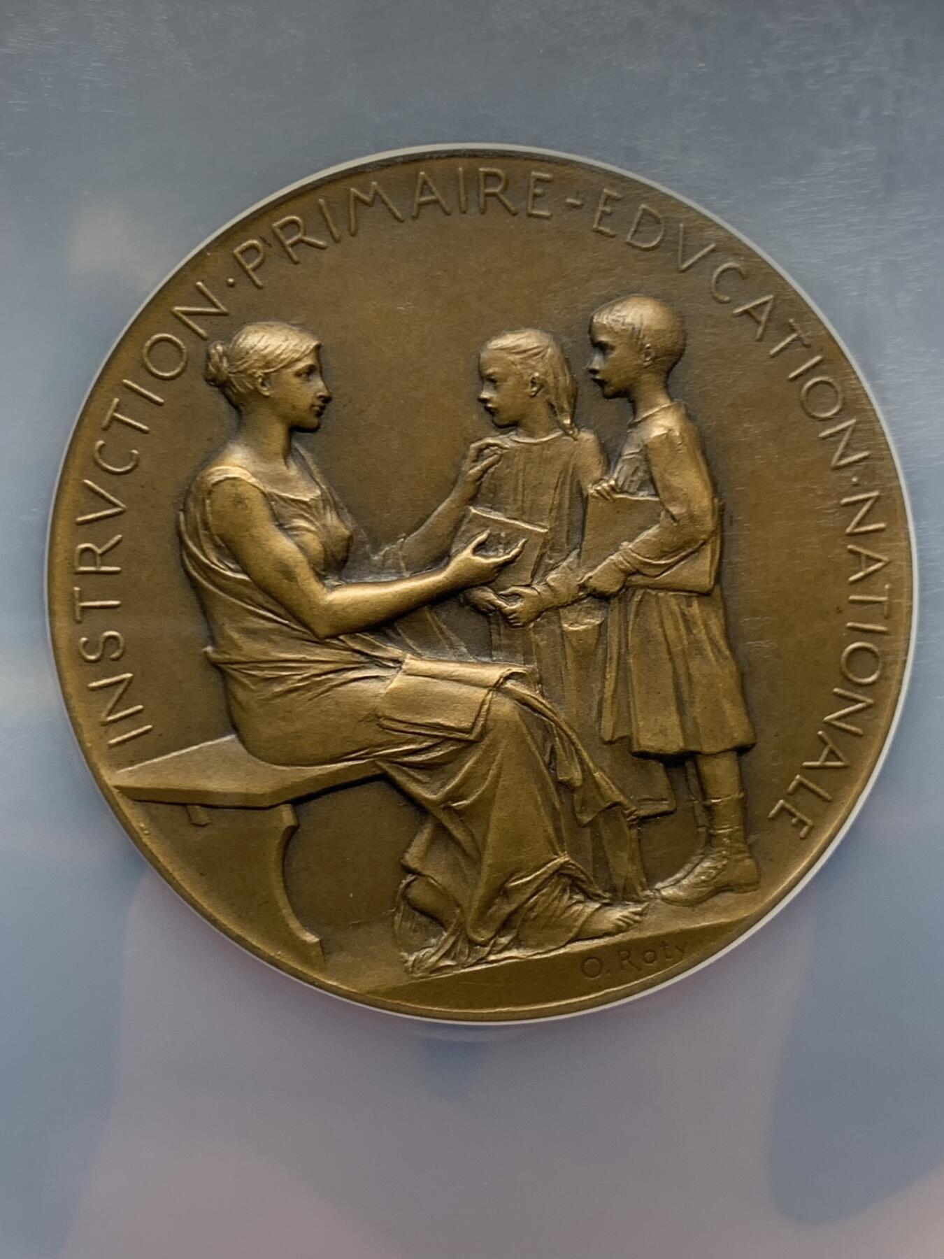 《竞宝斋》第465场 周日，周一，周二，3场连拍 （全场包邮）欢迎送拍 NGC MS64BN 1904年法国初级教育铜章，罗蒂作品，直径51毫米，正面图案展现了一位女性教师向两名学生传授知识的场景，象征着国家对基础教育的重视。加大盒