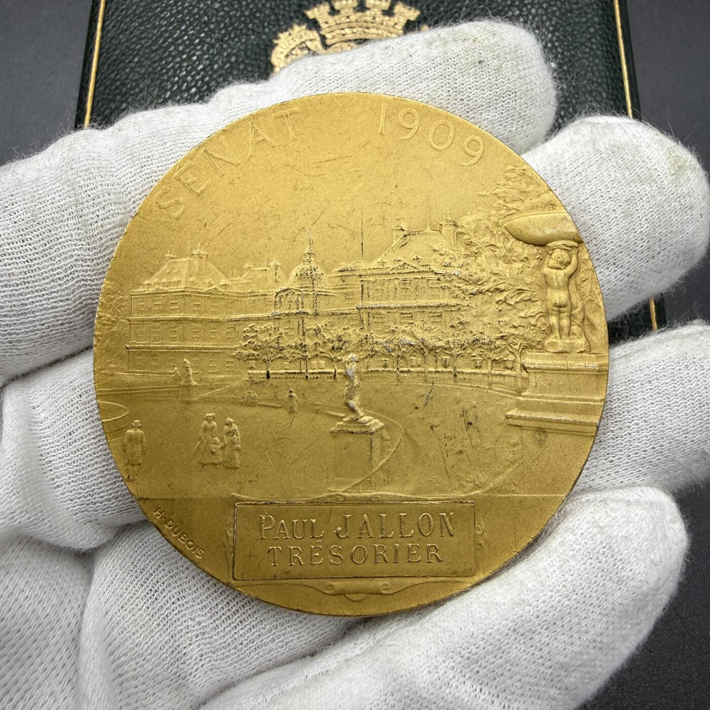 「木头集藏」“ 新岁撷珍”——章牌精品专场！ H. Dubois～1909年法国参议院议员镀金银章，直径：50mm，66 g，边铭：丰饶角 1ARGENT，品相不错，授予1909年担任法国参议院司库的保罗·雅隆（Paul Jallon）。正面刻画象征法兰西共和国的玛丽安娜凌空飞翔在法国参议院议事大厅之上，议员们坐在席位上，前方是演讲台，台下还有密集的旁听人群，还原了当时参议院的议事氛围。背面卢森堡宫 法国参议院所在地，烫金皮盒正常使用！