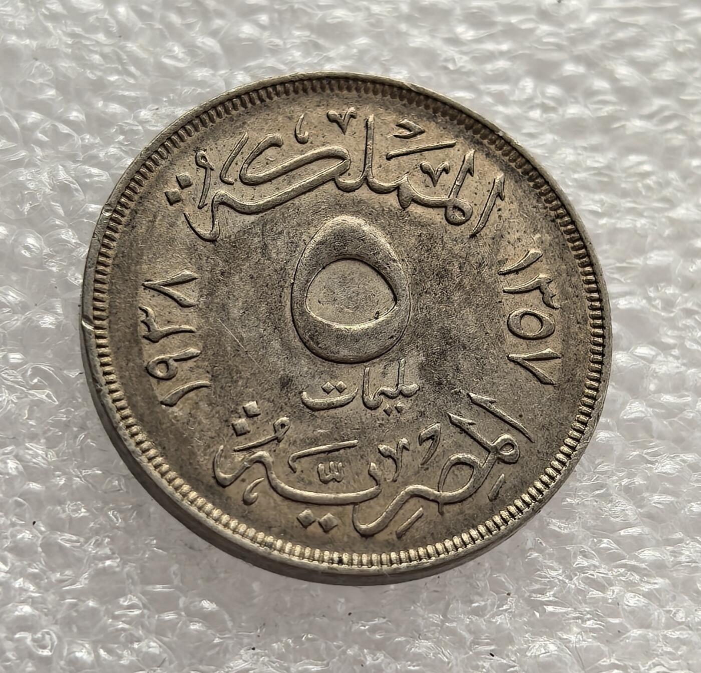 外国优质老铜币高银银币，周六九点倒数截拍，满百包邮，持续收拍，年后发货 埃及王国1938 年5米利姆，属于法鲁克一世统治时期的流通货币。当时埃及正处于从英国保护国向独立国家过渡的阶段，币面的君主头像与阿拉伯文设计，见证了殖民影响与本土文化交融下的货币体系建设。