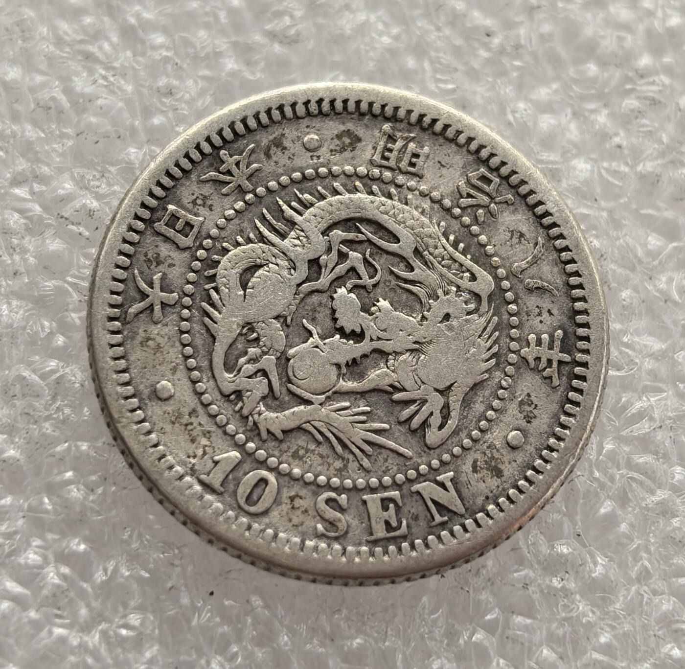 外国优质老铜币高银银币，周六九点倒数截拍，满百包邮，持续收拍，年后发货 日本明治八年（1875 年）  十钱银币，属于明治维新时期的流通货币。币面的龙纹与菊花纹章，是日本近代化转型的象征，反映了当时日本学习西方货币制度、推动经济工业化的努力，是明治维新后货币体系改革的重要见证。