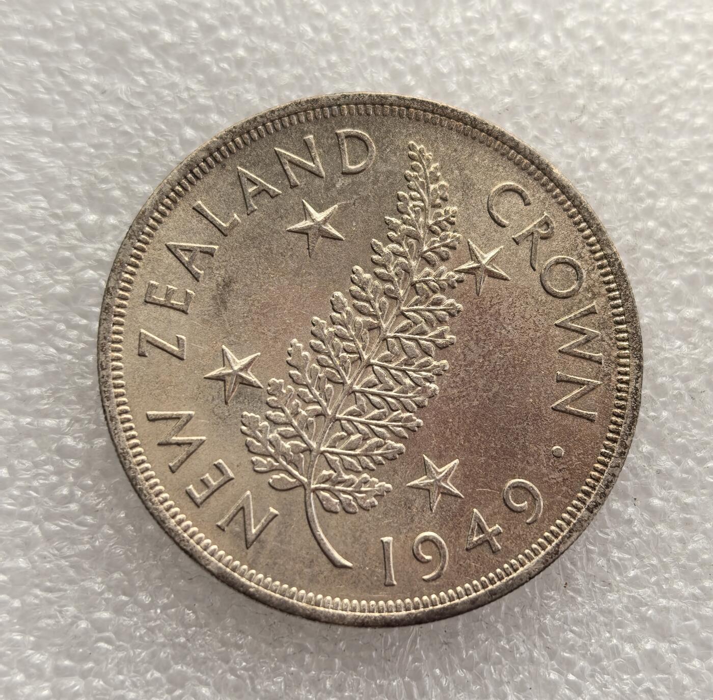 外国优质老铜币高银银币，周六九点倒数截拍，满百包邮，持续收拍，年后发货 新西兰 1949 年1 克朗银币，为纪念英王乔治六世计划出访新西兰而铸造。因国王健康恶化，出访取消，该币成为一场 “未发生的皇家访问” 的纪念物，以银质打造，正面为乔治六世像，背面是新西兰国树银蕨与星纹。