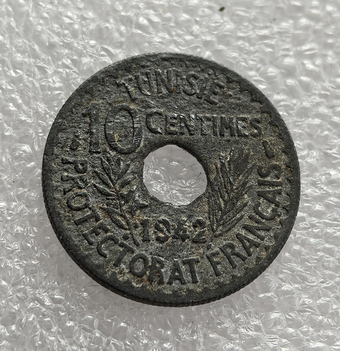 外国优质老铜币高银银币，周六九点倒数截拍，满百包邮，持续收拍，年后发货 法属突尼斯保护国 1942 年   10 生丁锌币，正值二战北非战场激战时期。当时突尼斯受战时物资短缺影响，以廉价锌铸币，中间圆孔是小额硬币典型设计，一面法语标识殖民身份，另一面阿拉伯文呼应本土文化，见证了殖民统治与战时经济的双重历史。