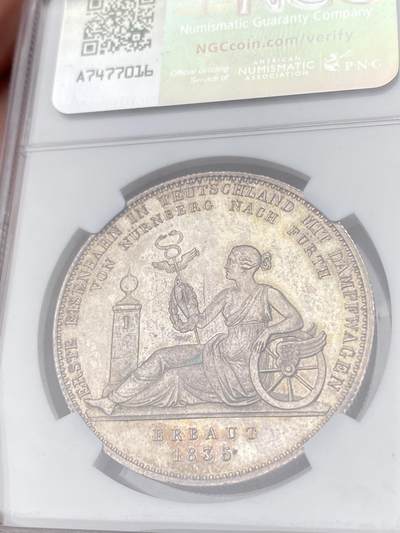 万国钱币拍卖第061期（马年首拍） NGC MS62 1835年德国巴伐利亚路德维希一世纪念巴伐利亚第一条蒸汽铁路开通纪念大泰勒 为了庆祝1835年纽伦堡到菲尔特的德国第一条蒸汽铁路开通 路德维希一世敕令发行此枚历史泰勒加以纪念 象征巴伐利亚的女神扶靠于双翅之轮上 手持墨丘利权杖与月桂花环 女神脚边石柱上的圆锥球是一种计时工具 预示列车准时准点 历史泰勒中的高难罕见品种 原味优雅清灰淡彩极美收藏级