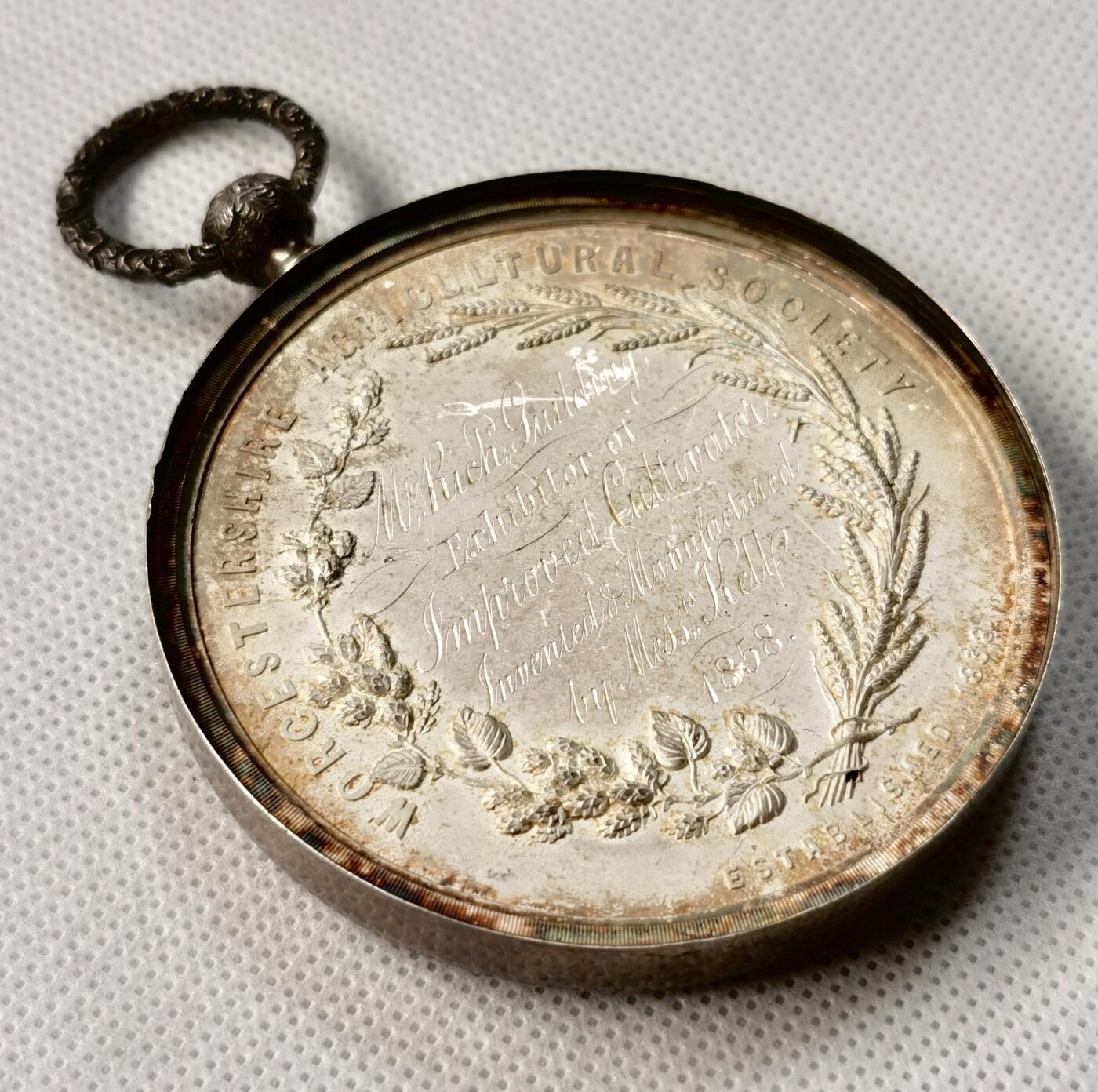 “福币呈祥”新年甄品场（直播拍卖）甄臻铺-世界币章拍卖（第50期），送拍享返佣金等优惠多多 1858年英国Worcestershire农业协会银质奖章，直径65毫米，重122克，反面玻璃罩丢失，全网农业玻璃罩章牌最大尺寸，雕工也是最精致传神的，好一幅勃勃生机的农业画卷啊。正面高浮雕农庄、牛、马、猪、羊等农畜，背面麦穗花环环绕协会名称和年份。由OTTLEY大师雕刻