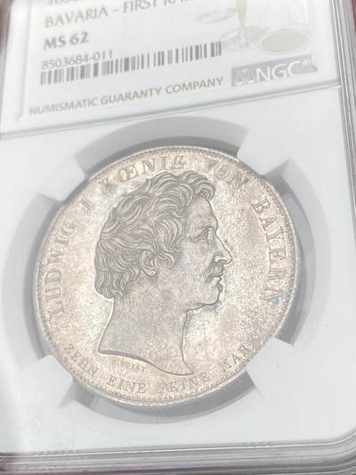 万国钱币拍卖第061期（马年首拍） NGC MS62 1835年德国巴伐利亚路德维希一世纪念巴伐利亚第一条蒸汽铁路开通纪念大泰勒 为了庆祝1835年纽伦堡到菲尔特的德国第一条蒸汽铁路开通 路德维希一世敕令发行此枚历史泰勒加以纪念 象征巴伐利亚的女神扶靠于双翅之轮上 手持墨丘利权杖与月桂花环 女神脚边石柱上的圆锥球是一种计时工具 预示列车准时准点 历史泰勒中的高难罕见品种 原味优雅清灰淡彩极美收藏级