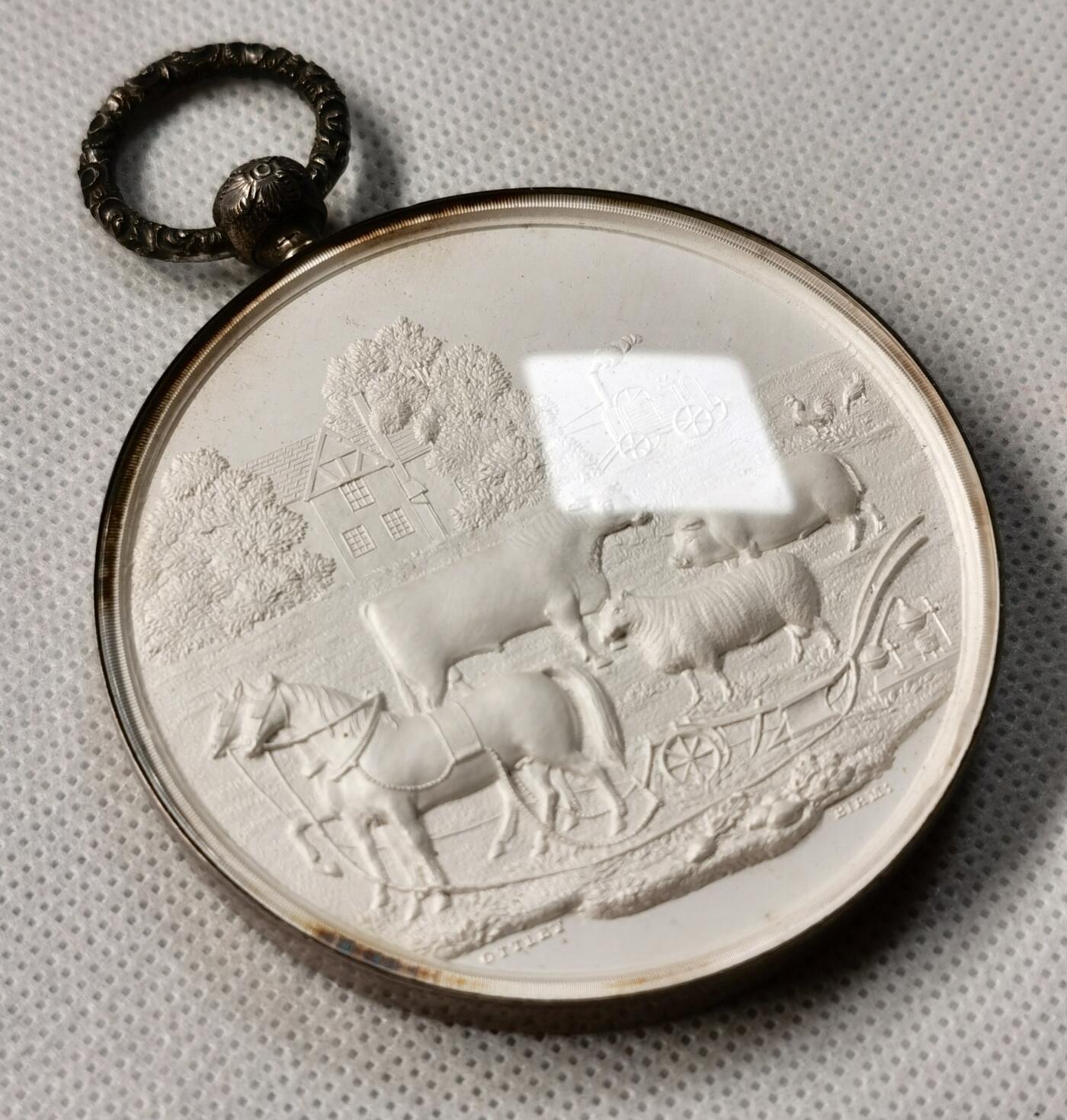 “福币呈祥”新年甄品场（直播拍卖）甄臻铺-世界币章拍卖（第50期），送拍享返佣金等优惠多多 1858年英国Worcestershire农业协会银质奖章，直径65毫米，重122克，反面玻璃罩丢失，全网农业玻璃罩章牌最大尺寸，雕工也是最精致传神的，好一幅勃勃生机的农业画卷啊。正面高浮雕农庄、牛、马、猪、羊等农畜，背面麦穗花环环绕协会名称和年份。由OTTLEY大师雕刻