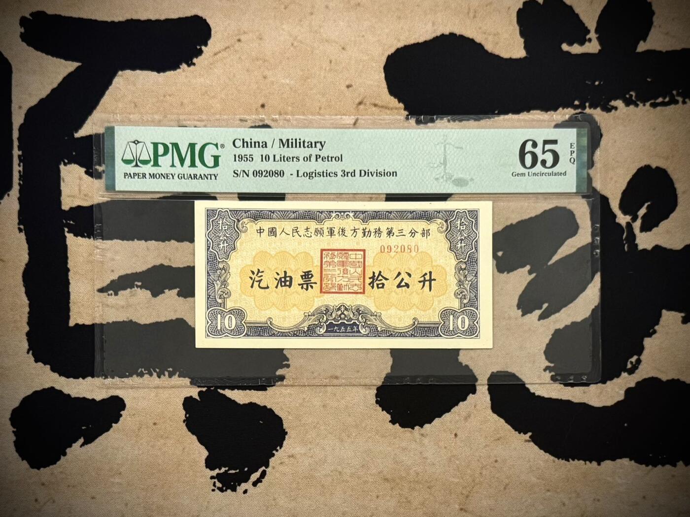 （自动截拍）PMG评级民国纸币专拍第20260219期，全场包邮  【乾奕收藏】1955年中国人民志愿军后方勤务第三分部汽油票拾公升，美国PMG65E，号码全程无13457朦胧号，这张汽油票发行于1955年，此时抗美援朝战争已经结束（1953年停战），但中国人民志愿军仍在朝鲜境内执行任务，需要统一的后勤保障体系。用于在志愿军内部兑换汽油，是当时军队后勤管理的重要凭证，反映了志愿军在朝鲜的物资调配体系