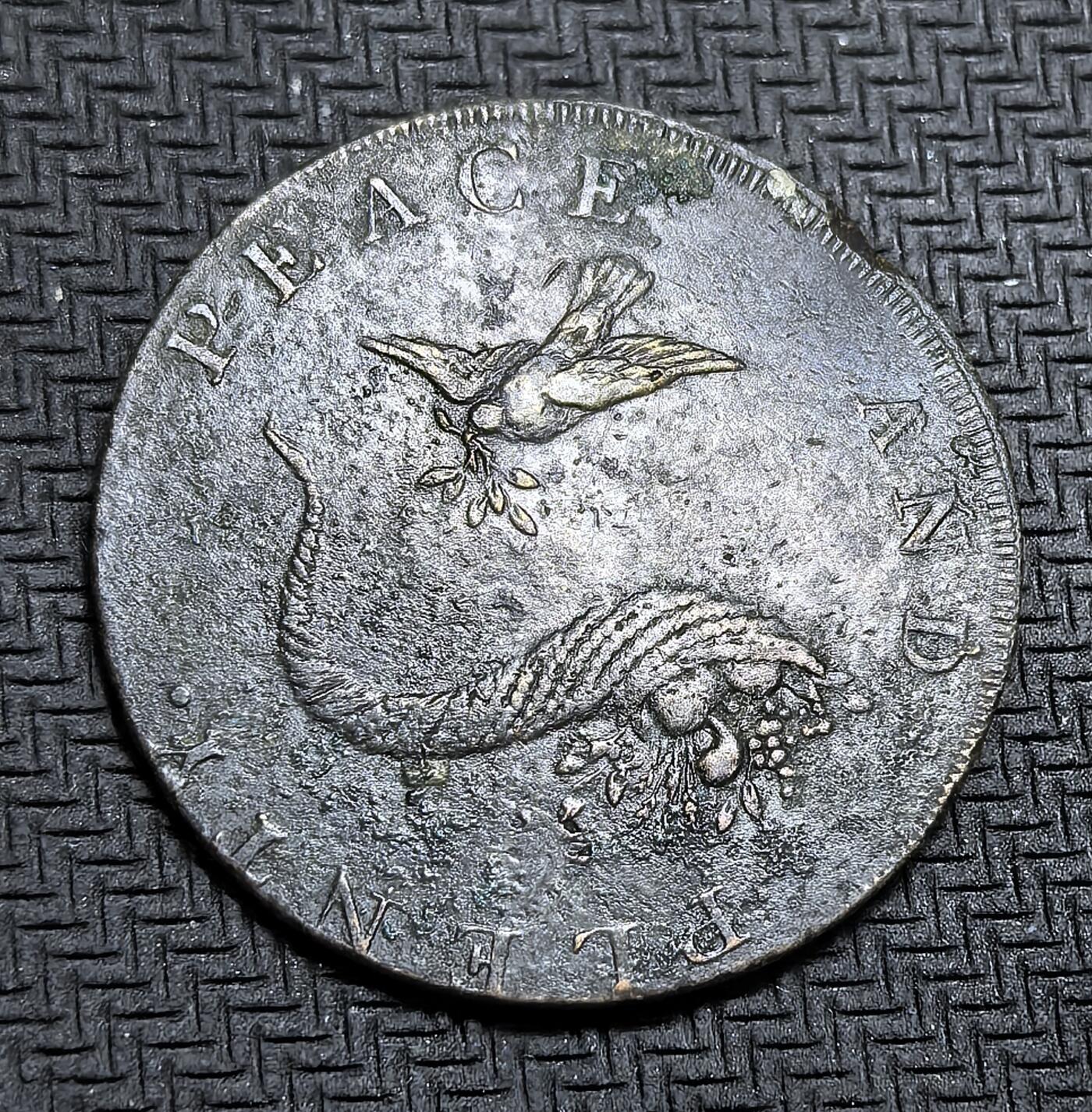 外国优质老铜币银币，周日九点倒数截拍，满百包邮，持续收拍，初八发货 图案清晰英国1793年半便士代用币。正面刻有和平与丰饶，衔着橄榄枝的鸽子与丰饶角图案，寄托了对和平与富足的期盼；背面的 “HALFPENNY” 与 1793 年字样，以及象征商业与海洋的坐像、锚和狮子，反映了工业革命初期英国的经济活力与殖民野心。这枚代用币是地方发行的私铸货币，用于缓解当时官方货币短缺的困境。虽然图案清晰但是币有不平边翘。