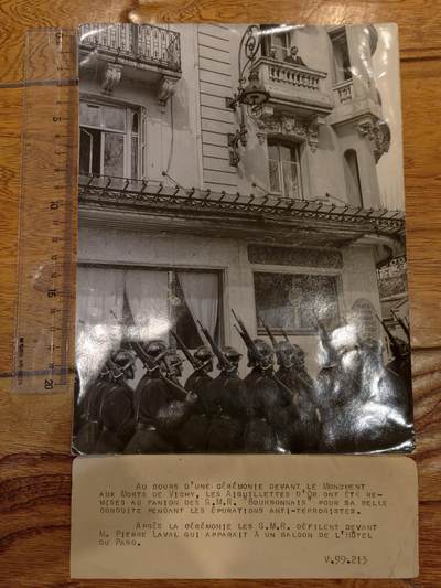 凯旋世界勋赏（持续上新中）（第22期新年大拍）（欢迎送拍）（对拍品有疑问请询问客服，不接受到手刀，出价默认拍品品相。请认真阅读拍卖规则！出价默认已认可！）（收到货请录制开箱视频，无视频概不处理问题。） - 地点：维希市的 Hôtel du Parc（公园酒店）前，这是维希政权元首贝当元帅的官邸。  - 事件：仪式结束后，G.M.R.（武装预备军团）部队在公园酒店前游行，皮埃尔·拉瓦尔（Pierre Laval）出现在酒店的阳台上。  - 细节：照片中可以看到整齐列队的武装士兵，手持步枪，步伐统一，仪式感强烈；酒店阳台上有人影，应为拉瓦尔及其随行人员。