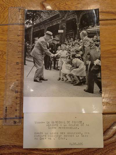 凯旋世界勋赏（持续上新中）（第22期新年大拍）（欢迎送拍）（对拍品有疑问请询问客服，不接受到手刀，出价默认拍品品相。请认真阅读拍卖规则！出价默认已认可！）（收到货请录制开箱视频，无视频概不处理问题。） - 维希市的一处官方场所（应为公园酒店前的观礼台）。  - 事件：贝当元帅在出席私人卫队换岗仪式后，俯身与围栏外的儿童握手互动，孩子们簇拥在他身边，画面刻意营造出温馨亲民的氛围