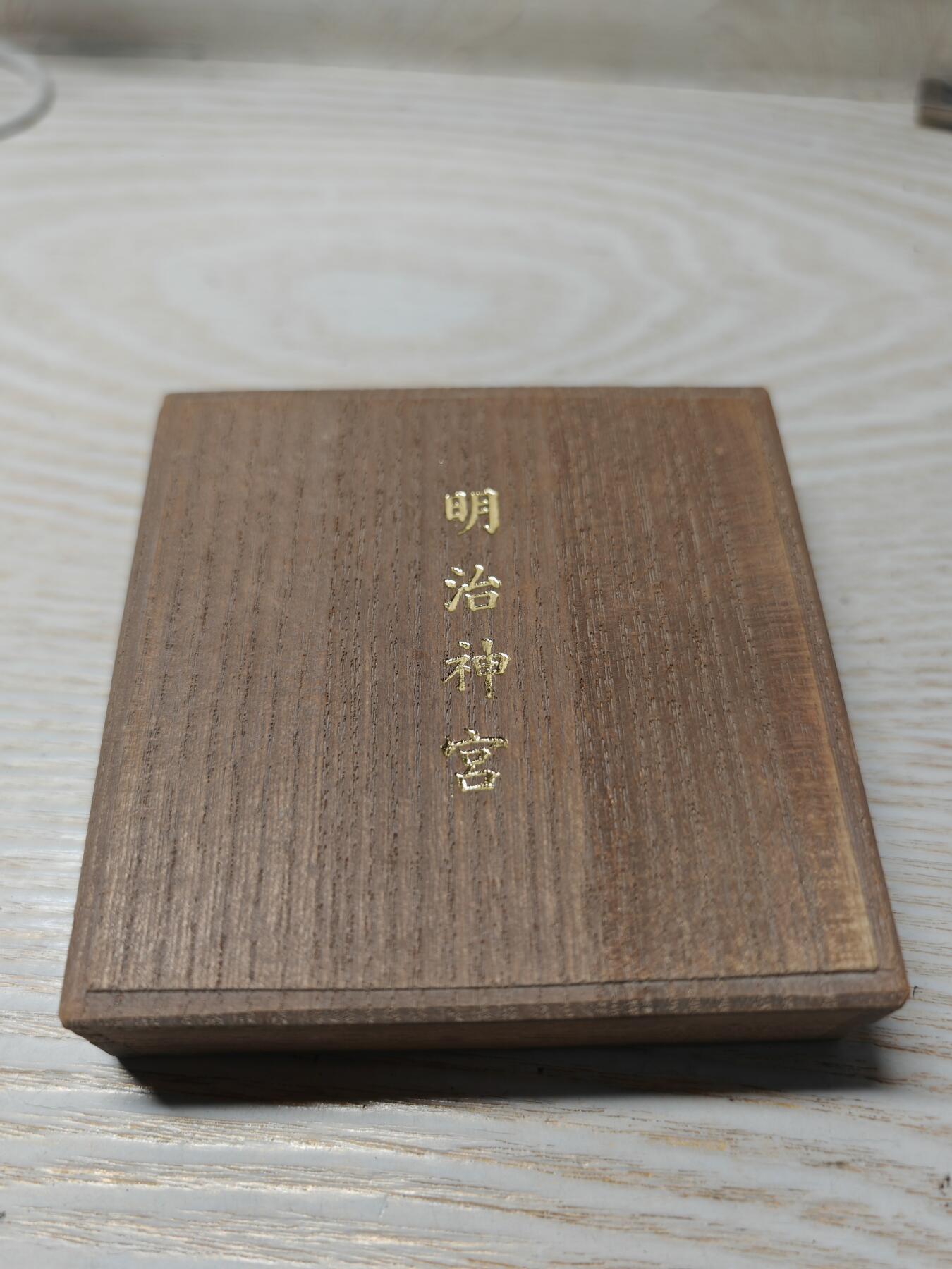 日本明治神宮的铜制纪念章 中央是双凤凰相对而立，周围环绕着菊花、牡丹等花卉纹样，顶部是日本皇室的十六瓣八重表菊纹。 背面是明治天皇的御制和歌，大意是：“在您的光辉下，朝阳格外耀眼；为了您，我心怀清爽而思念。