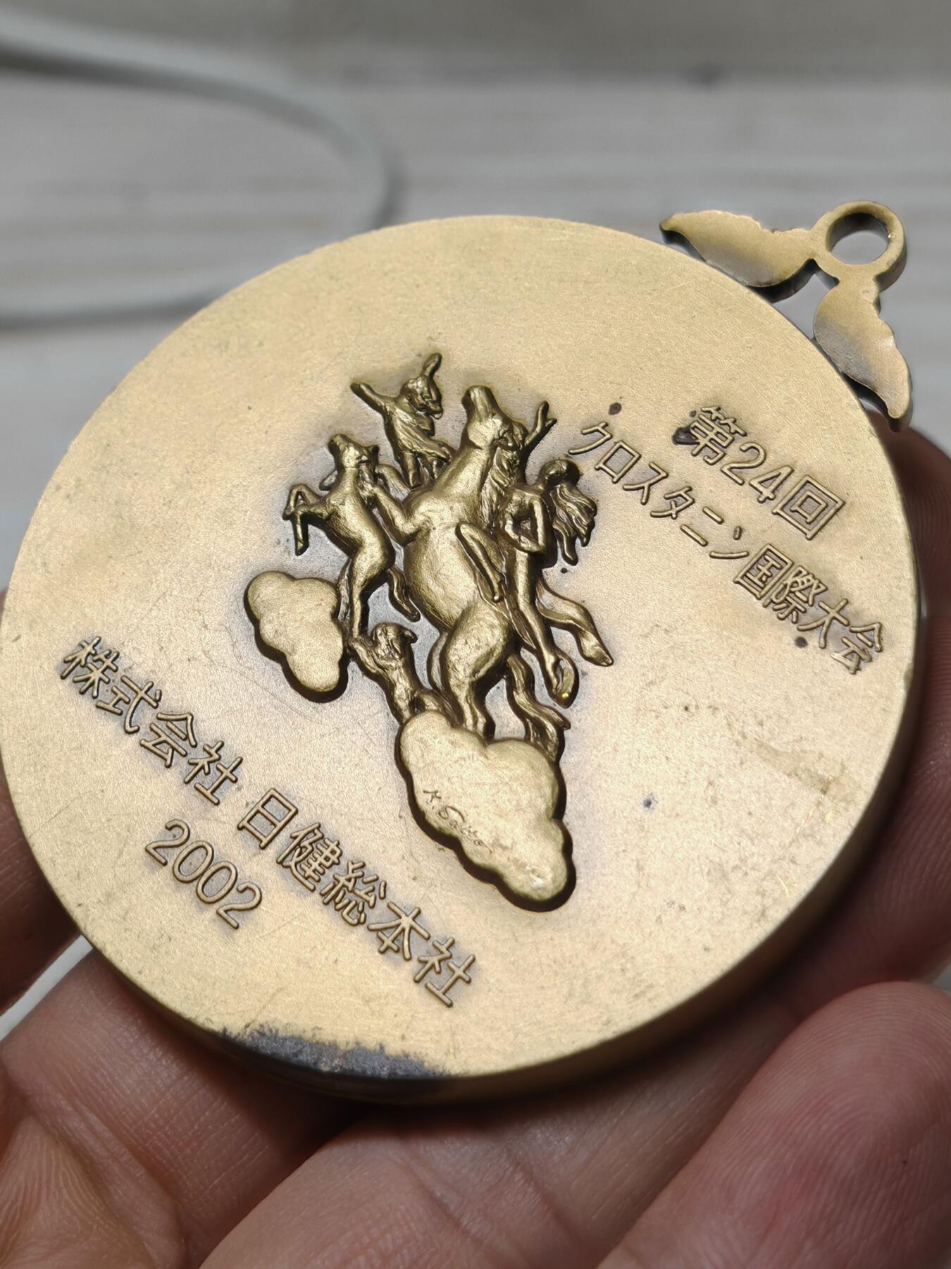 2002年第24届克罗斯塔宁国际大会纪念奖牌人物立体 - 正面：浮雕为日健総本社的创始人田中美穂的头像，右下角有雕刻师签名。 - 背面：刻有“第24回クロスタニン国際大会”、“株式会社 日健総本社”和年份“2002”，并配有飞马与人物的神话风格浮雕。 浮雕工艺精细，背面的飞马神话图案设计独特，具有一定的艺术观赏性。