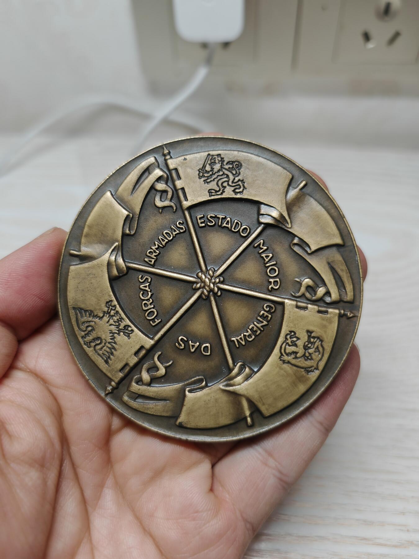 葡萄牙少见军事题材纪念铜章 - 主图案：葡萄牙传统的持剑双头鹰盾徽，这是葡萄牙军事机构的经典象征，代表着指挥权与历史传承。 - 工艺特征：采用高浮雕工艺，整个设计体现了陆、海、空三军的统一指挥与协调，是葡萄牙军事体系的核心象征。