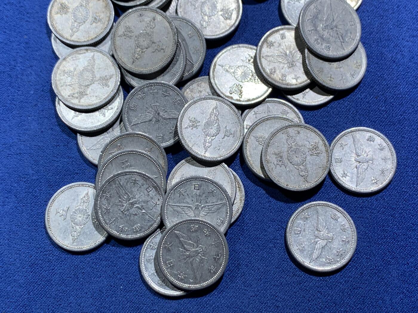 《竞宝斋》第466场 周日，周一 2场连拍 （全场包邮）欢迎送拍 54枚一组 日本战时1940-1943年飞鸟（金鵄）五钱铝制硬币，彼时日本深陷战争泥潭，原本的铜质五钱被迫停产改为铝币，该币正面是日本皇室的十六瓣八重表菊纹，外环镌刻国号与昭和年号；背面主体为象征日本的金鵄（飞鸟）图案，搭配“五钱”面值，1943年因铝资源彻底枯竭停铸。