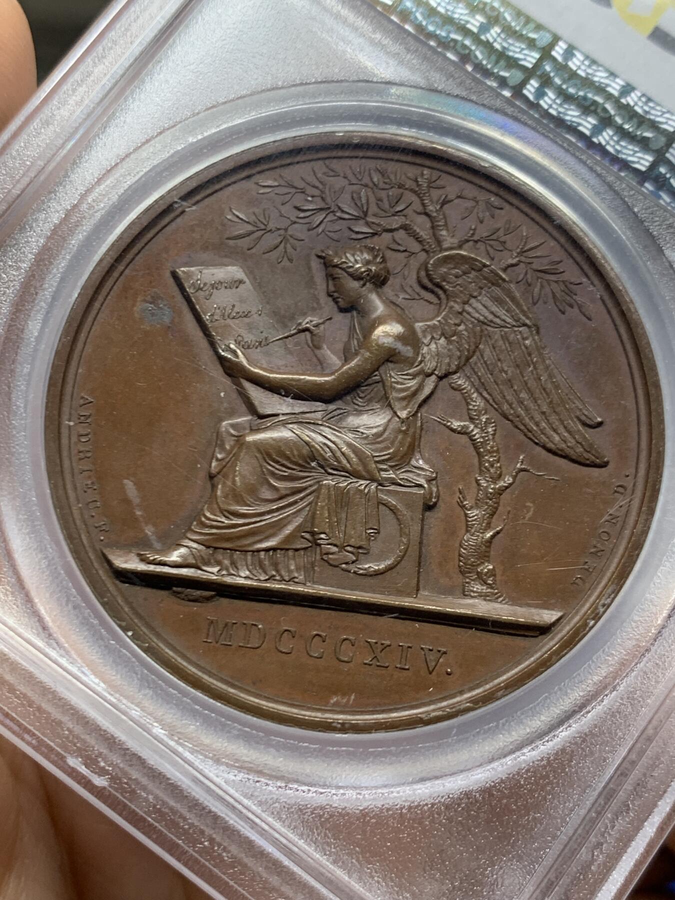 《竞宝斋》第466场 周日，周一 2场连拍 （全场包邮）欢迎送拍 PCGS SP64 亚军分 法国1814年沙皇亚历山大一世访问巴黎铜章 正面沙皇月桂冠高浮雕，完全拿章典型风格头像，背面天使坐于树荫下书写历史，纪念沙皇占领期访巴黎造币厂，第六次反法同盟胜利，法兰西第一帝国覆灭，拿皇退位流放，巴黎由俄军掌管。作为胜利者的沙皇骑着白马率大军通过凯旋门，不知他是否满脑一年前拿皇攻占莫斯科场景，与其说“访问巴黎”，不如说彰显复仇拿皇的耀武扬威。加厚盒