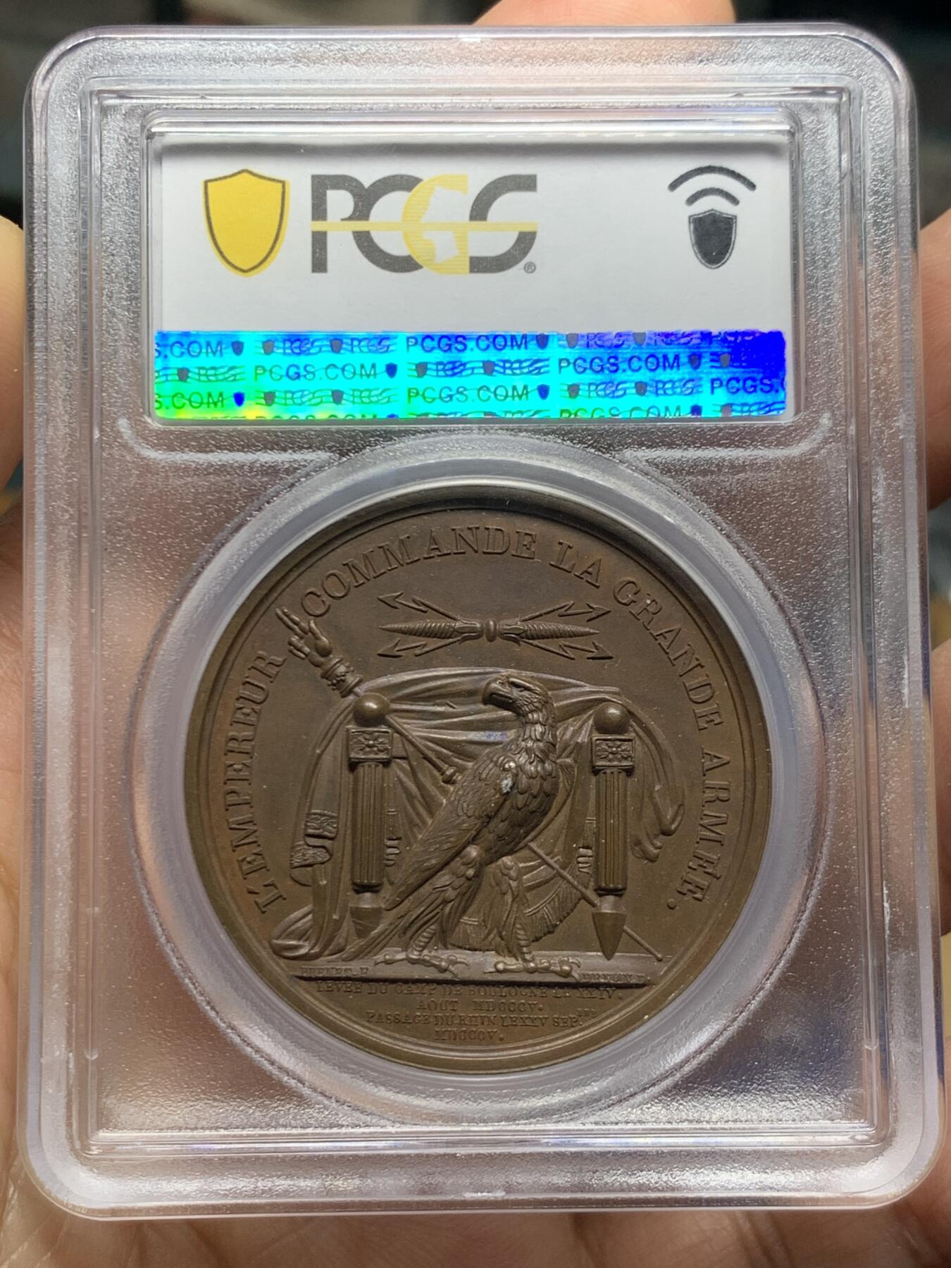 《竞宝斋》第467场 周日，周一 2场连拍 （全场包邮）欢迎送拍 PCGS SP64 亚军分！法国1805年拿破仑布洛涅大营原铸铜章 巴黎造币厂 巧克力包浆，王座上覆着拿皇加冕时的披风，帝国鹰坐于王座前目不转睛直盯着王座上方斜放的正义之手权杖，上方是一束闪电。传奇的布洛涅大营位于法国滨海，第一个营地由凯撒于公元前54年准备，为远征不列颠做准备舰队，第二个营地由拿破仑1803年建立，他在那里组建了“大军”，即海洋军，准备入侵英国，无愧凯撒的光荣传承人。加厚盒装