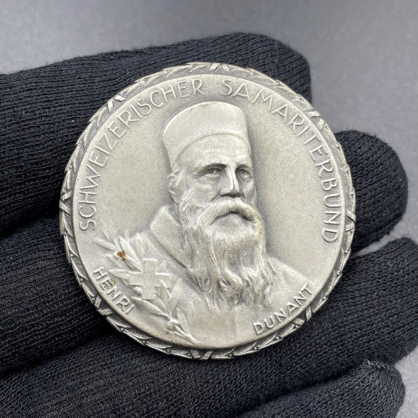 「木头集藏」章牌专场-第69场 Huguenin Frères～1965年瑞士红十字会撒玛利亚人联合会银章。直径：42mm，50.1g，背面下方标有含银量0.925和厂标HF，边缘的花边设计很有特色。  正面肖像是“红十字会之父”亨利·杜南（Henri Dunant，1828-1910年），他在1863年促成了国际红十字会的创立，1864年的《日内瓦公约》也是以他的思想为基础。