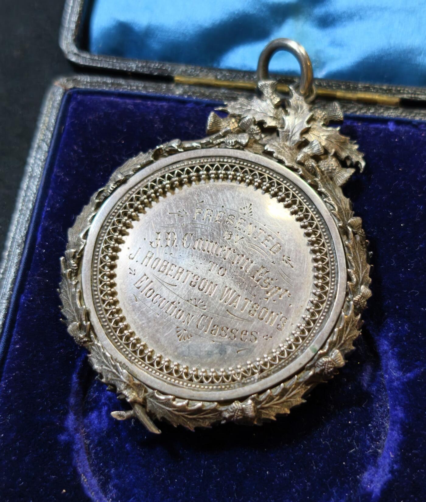 甄臻铺-世界币章拍卖（第53期），甄品场拍品征集中，送拍享返佣金等优惠多多 1895年英国J.D. Cameron Esq.颁发的银质奖章，重46.9克，尺寸72.5x55x7.3毫米，带原装皮盒，环绕花环装饰，英国装饰主义复杂银饰工艺典范，包浆自然