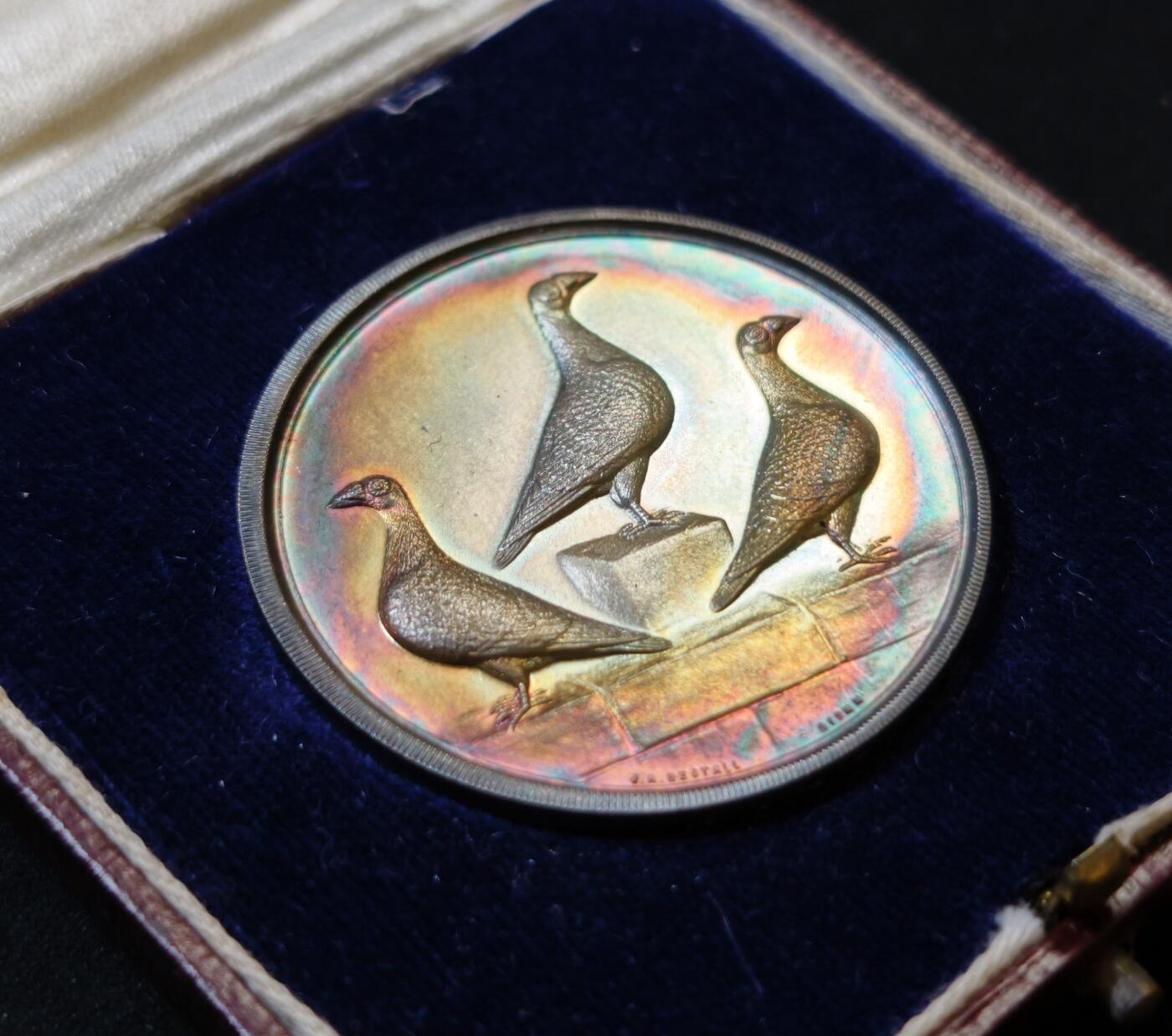 甄臻铺-世界币章拍卖（第53期），甄品场拍品征集中，送拍享返佣金等优惠多多 1927年英国龙骑士赛鸽俱乐部获奖银章，直径39毫米，重32克。正面雕刻三只鸽子图案，背面刻有W.H.Inman获奖字样。原装红皮盒，带内衬丝绒垫。表面自然氧化呈现五彩包浆，工艺精湛。边缘清晰，铭文完整，原装盒子完整