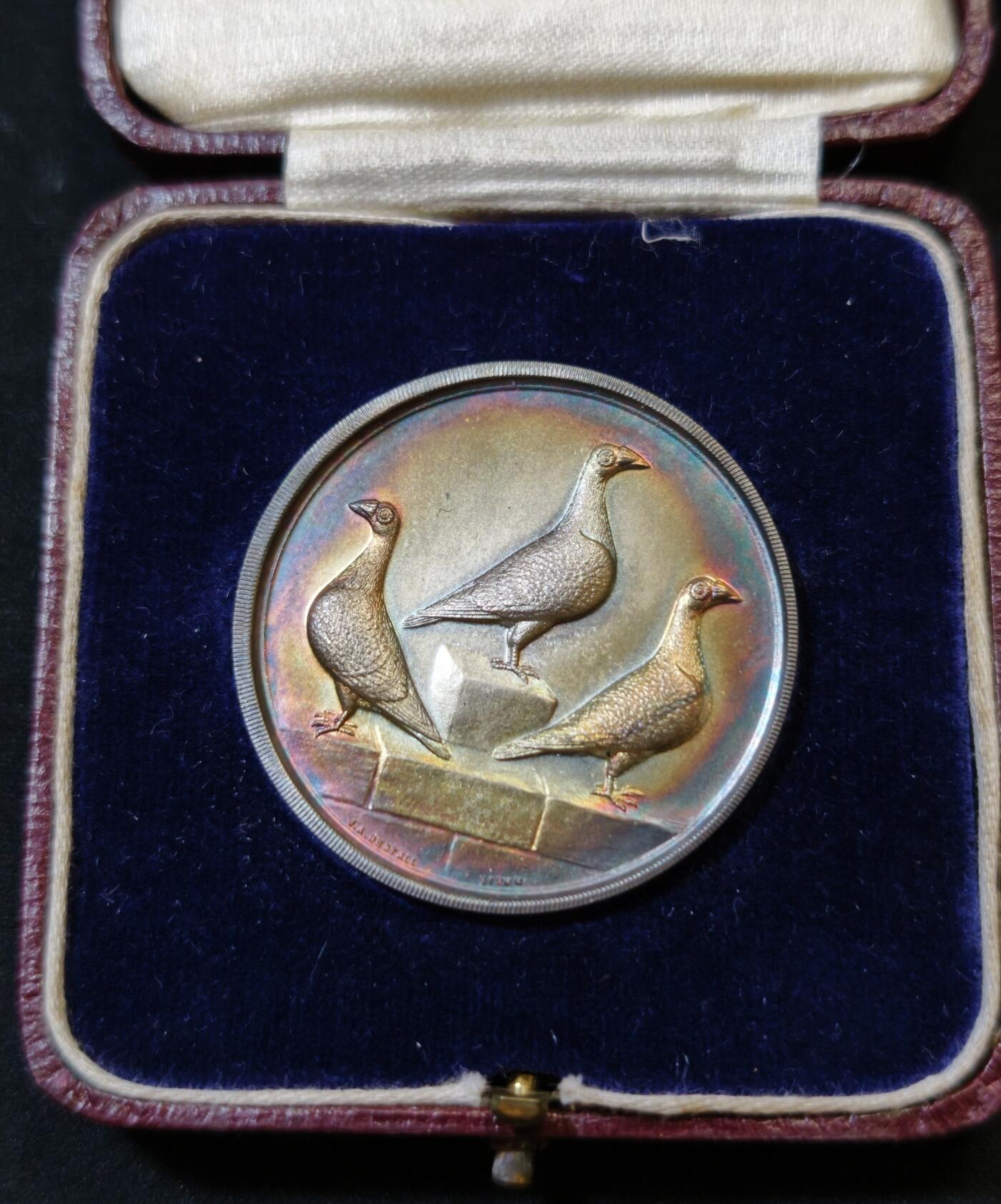 甄臻铺-世界币章拍卖（第53期），甄品场拍品征集中，送拍享返佣金等优惠多多 1927年英国龙骑士赛鸽俱乐部获奖银章，直径39毫米，重32克。正面雕刻三只鸽子图案，背面刻有W.H.Inman获奖字样。原装红皮盒，带内衬丝绒垫。表面自然氧化呈现五彩包浆，工艺精湛。边缘清晰，铭文完整，原装盒子完整