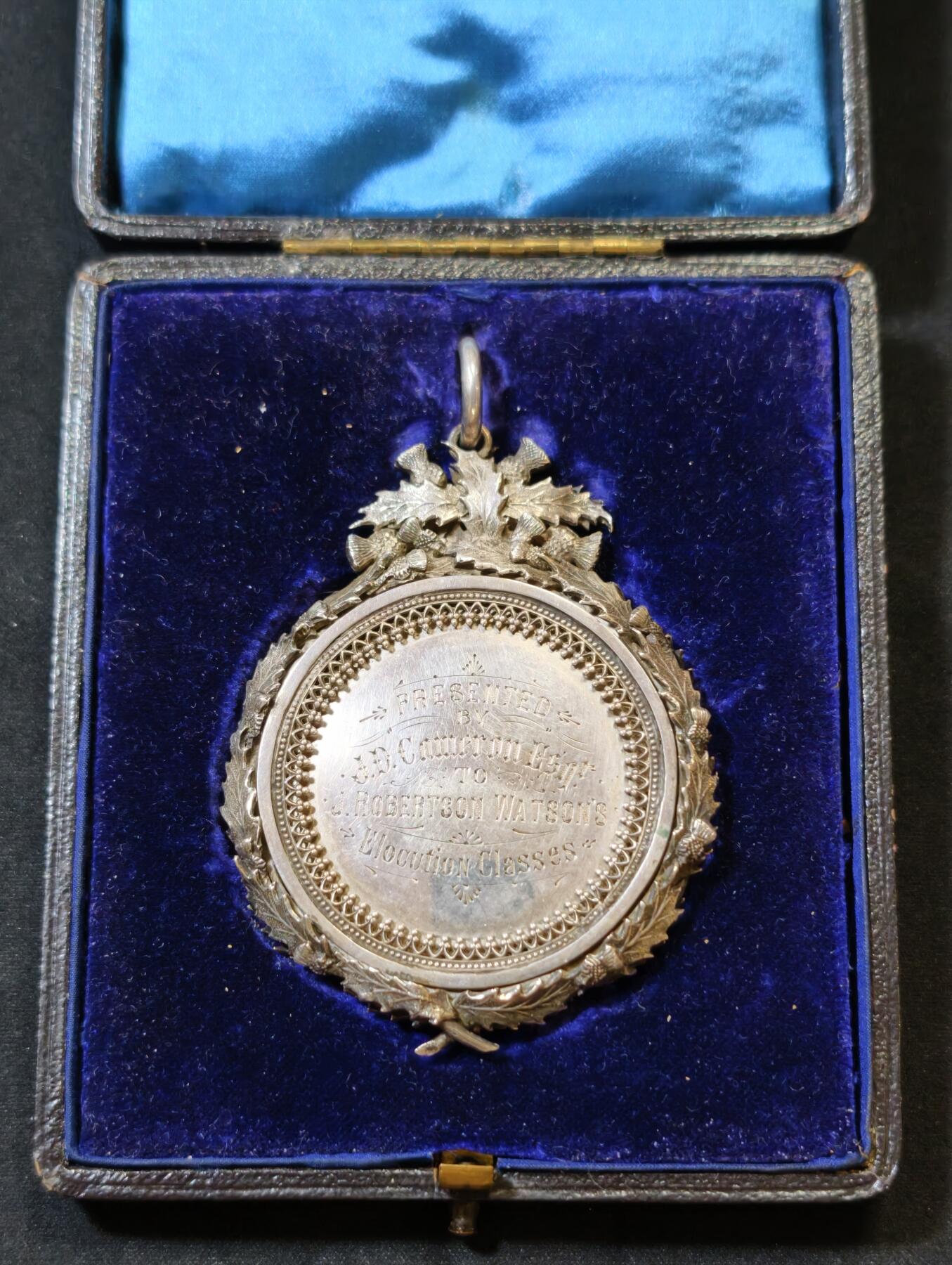 甄臻铺-世界币章拍卖（第53期），甄品场拍品征集中，送拍享返佣金等优惠多多 1895年英国J.D. Cameron Esq.颁发的银质奖章，重46.9克，尺寸72.5x55x7.3毫米，带原装皮盒，环绕花环装饰，英国装饰主义复杂银饰工艺典范，包浆自然