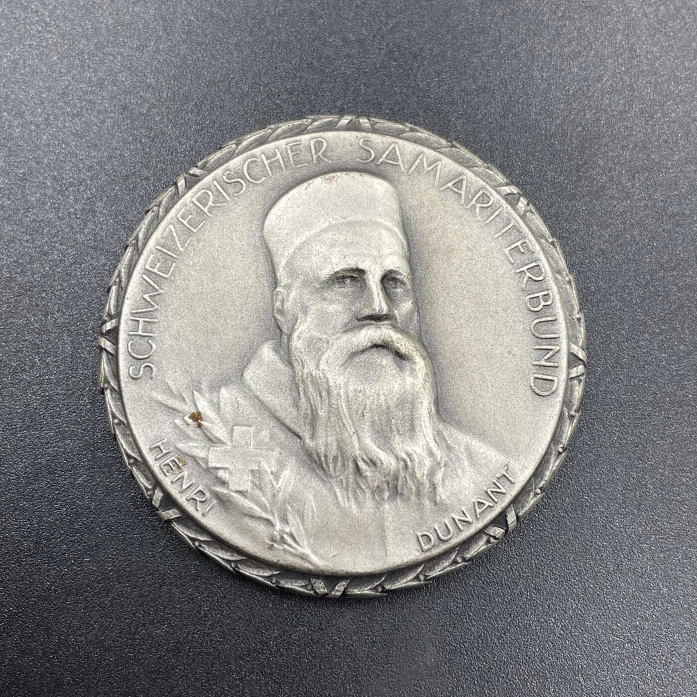 「木头集藏」章牌专场-第69场 Huguenin Frères～1965年瑞士红十字会撒玛利亚人联合会银章。直径：42mm，50.1g，背面下方标有含银量0.925和厂标HF，边缘的花边设计很有特色。  正面肖像是“红十字会之父”亨利·杜南（Henri Dunant，1828-1910年），他在1863年促成了国际红十字会的创立，1864年的《日内瓦公约》也是以他的思想为基础。