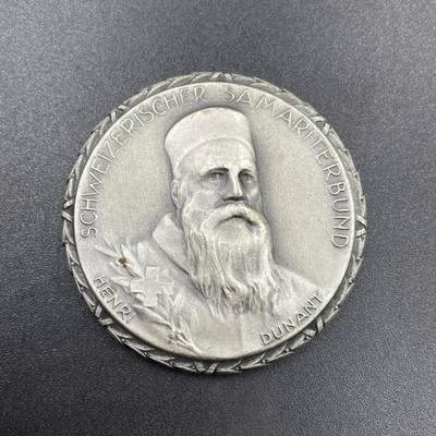 「木头集藏」章牌专场-第69场 - Huguenin Frères～1965年瑞士红十字会撒玛利亚人联合会银章。直径：42mm，50.1g，背面下方标有含银量0.925和厂标HF，边缘的花边设计很有特色。  正面肖像是“红十字会之父”亨利·杜南（Henri Dunant，1828-1910年），他在1863年促成了国际红十字会的创立，1864年的《日内瓦公约》也是以他的思想为基础。