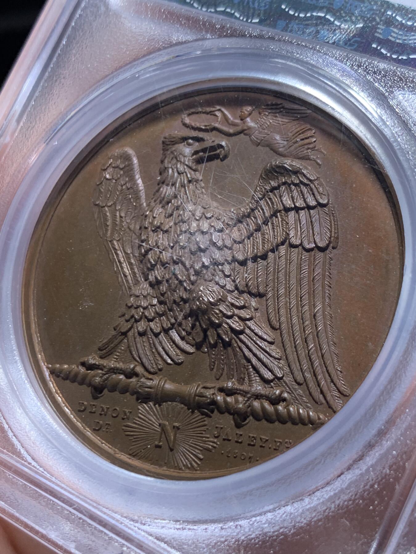 《竞宝斋》第469场 周日，周一 2场连拍 （全场包邮）欢迎送拍 PCGS SP65 冠军分！法国1807年拿破仑一世年度胜利原铸铜章 巴黎造币厂 巧克力包浆 帝国之鹰展翅爪子锋利 紧紧攥住矗立于N记雷电权杖之上 目光锐利如炬 羽翼丰满 丝缕清晰细节感人 作为拿皇的拟人化象征 接受上空胜利女神飞舞空中送来月桂花环为其加冕 作为年度总结庆祝过去的一年中军队获取的胜利 稀少珍贵品种 加厚盒