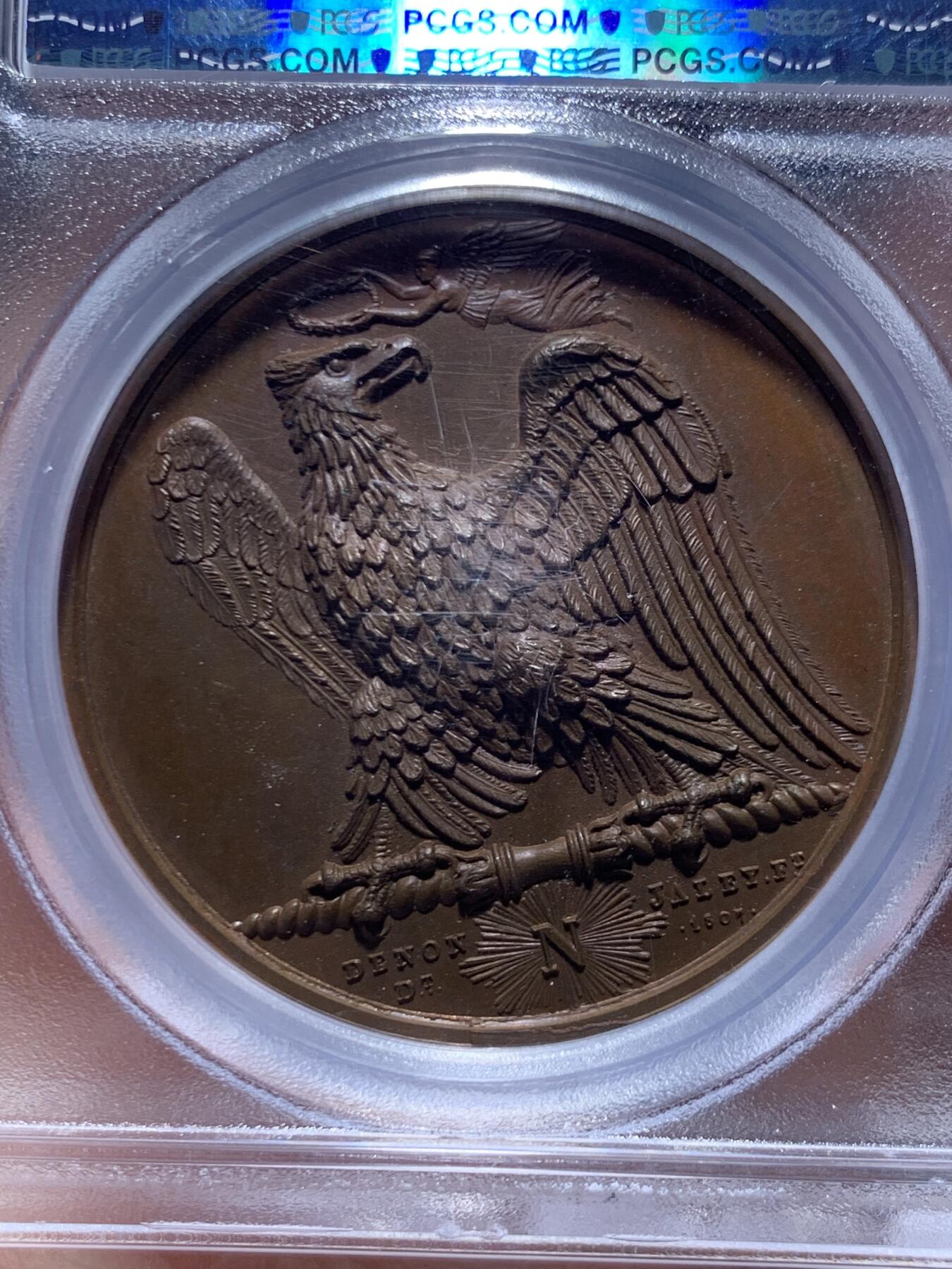 《竞宝斋》第469场 周日，周一 2场连拍 （全场包邮）欢迎送拍 PCGS SP65 冠军分！法国1807年拿破仑一世年度胜利原铸铜章 巴黎造币厂 巧克力包浆 帝国之鹰展翅爪子锋利 紧紧攥住矗立于N记雷电权杖之上 目光锐利如炬 羽翼丰满 丝缕清晰细节感人 作为拿皇的拟人化象征 接受上空胜利女神飞舞空中送来月桂花环为其加冕 作为年度总结庆祝过去的一年中军队获取的胜利 稀少珍贵品种 加厚盒