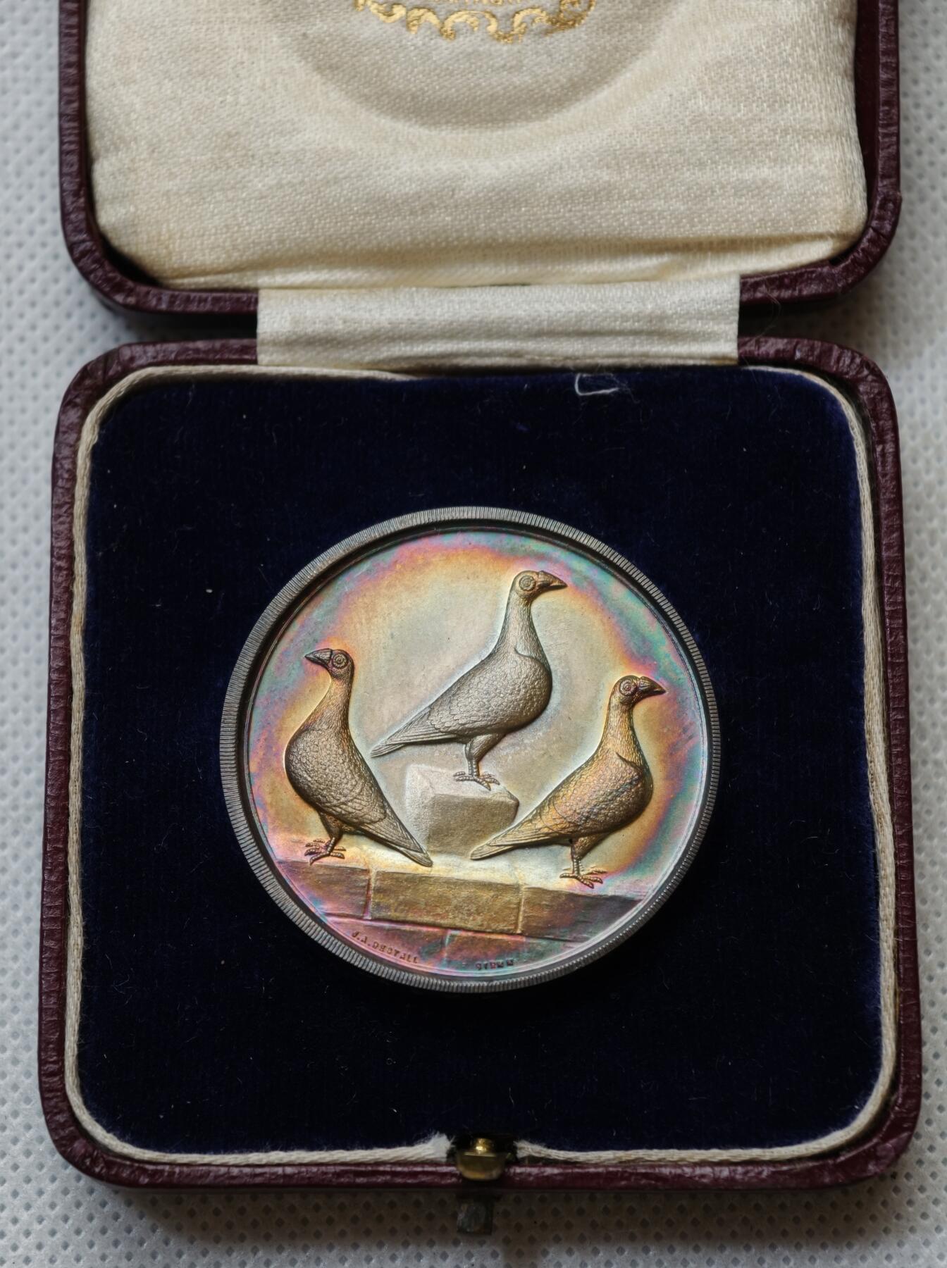 甄臻铺-世界币章拍卖（第54期），3月28日甄品场拍品征集中，送拍享返佣金等优惠多多 1927年英国龙骑士赛鸽俱乐部获奖银章，直径39毫米，重32克。正面雕刻三只鸽子图案，背面刻有W.H.Inman获奖字样。原装红皮盒，带内衬丝绒垫。表面自然氧化呈现五彩包浆，工艺精湛。边缘清晰，铭文完整，原装盒子完整（鸽子重拍）