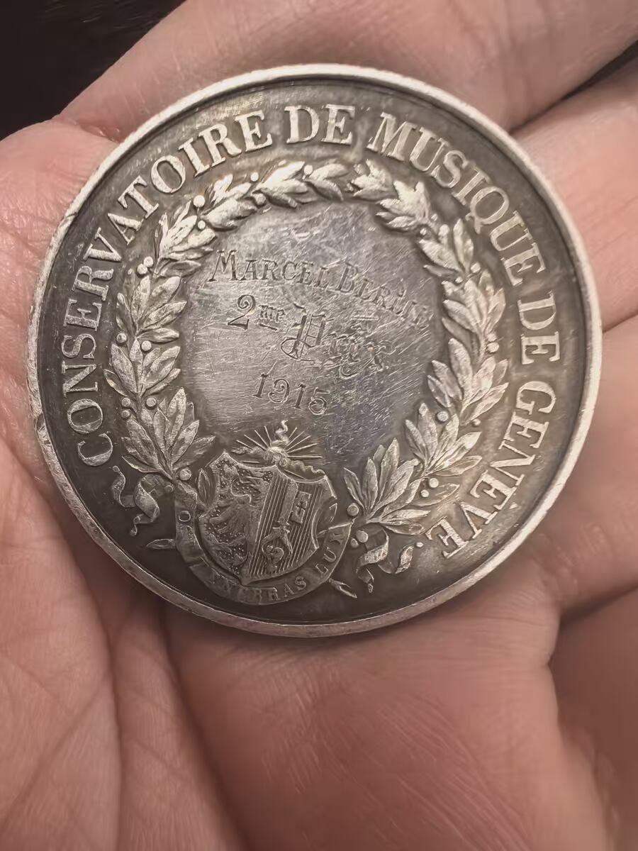 欧洲银章铜章、银币 日内瓦音乐学院银质纪念银章34.2克 这是一枚来自瑞士日内瓦音乐学院（Conservatoire de Musique de Genève）的银质纪念章，是为了表彰1915年的优秀学生Marcel Blouin而颁发的。 正面（Avers）二等奖